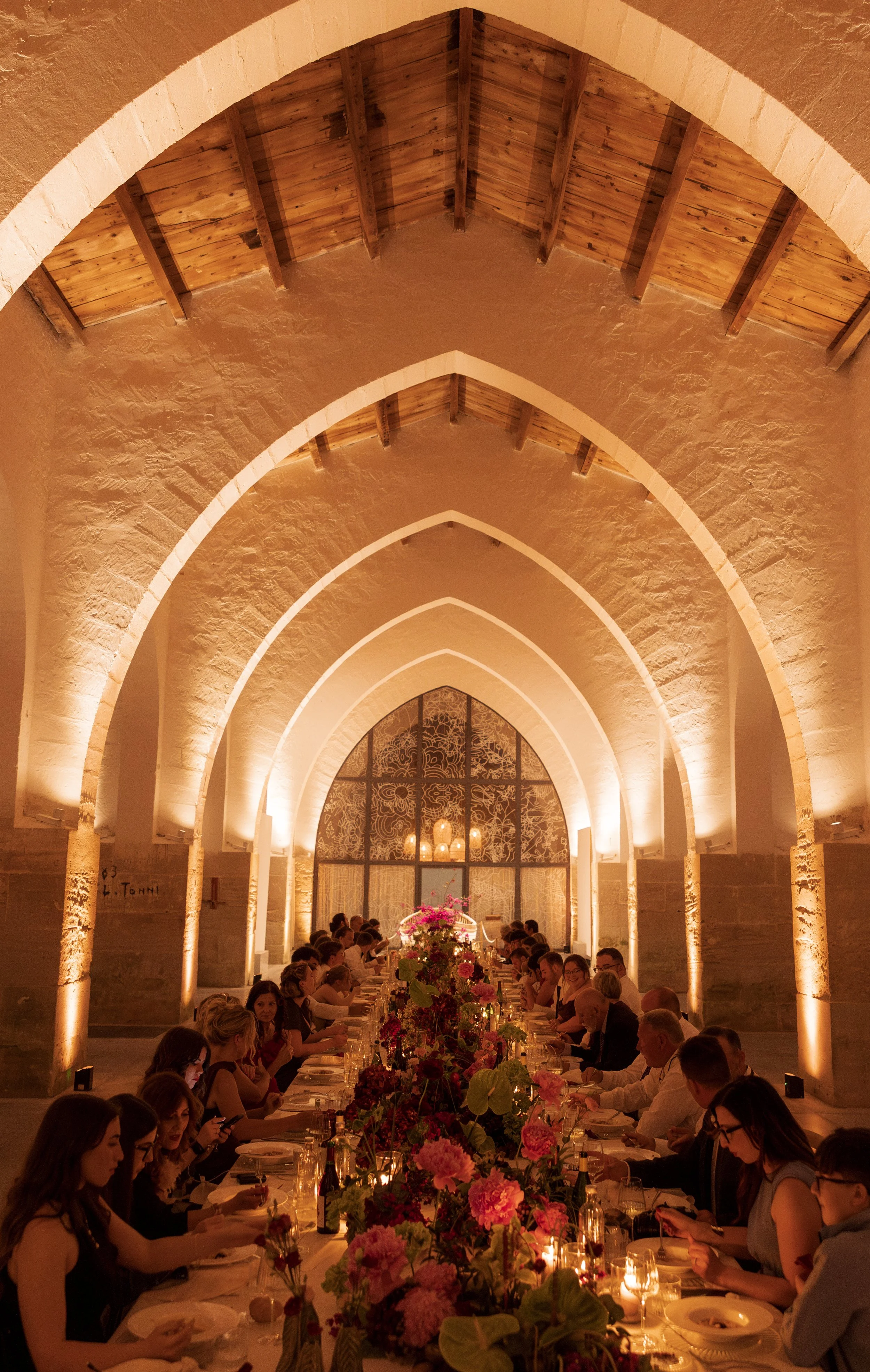 Editorial wedding photograph of a candlelit dinner beneath Camparia Favignana's illuminated stone arches, with guests seated along a floral reception table.