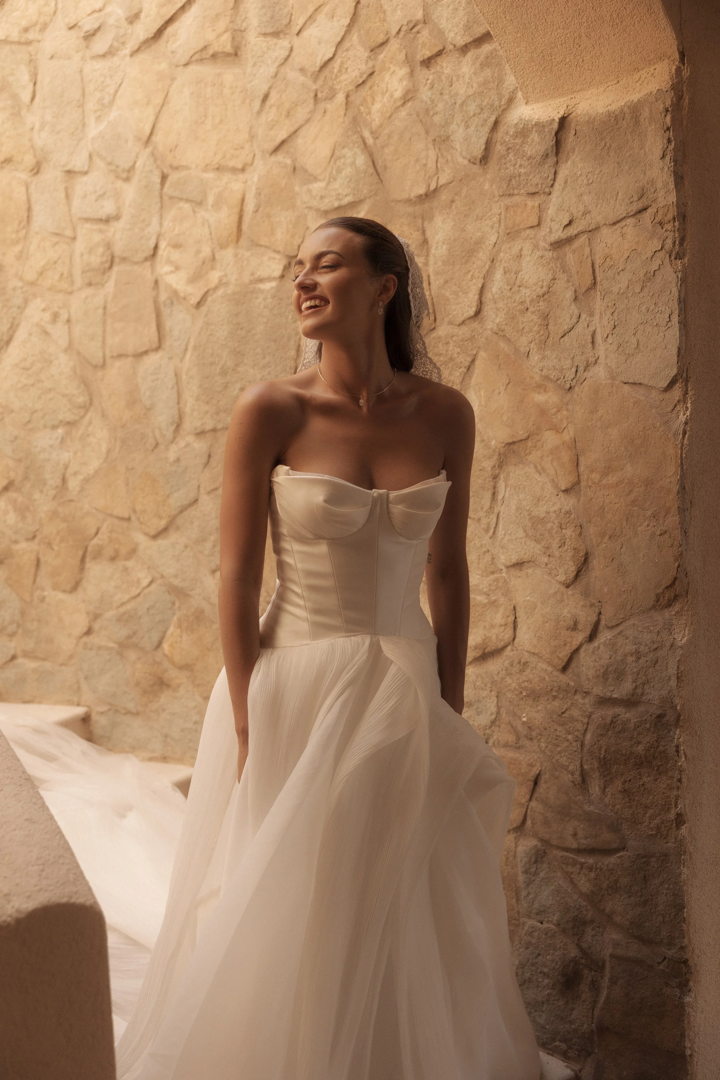 Editorial bridal photograph of Savannah wearing a strapless wedding gown and lace veil against warm stone walls during her Sicily destination wedding.
