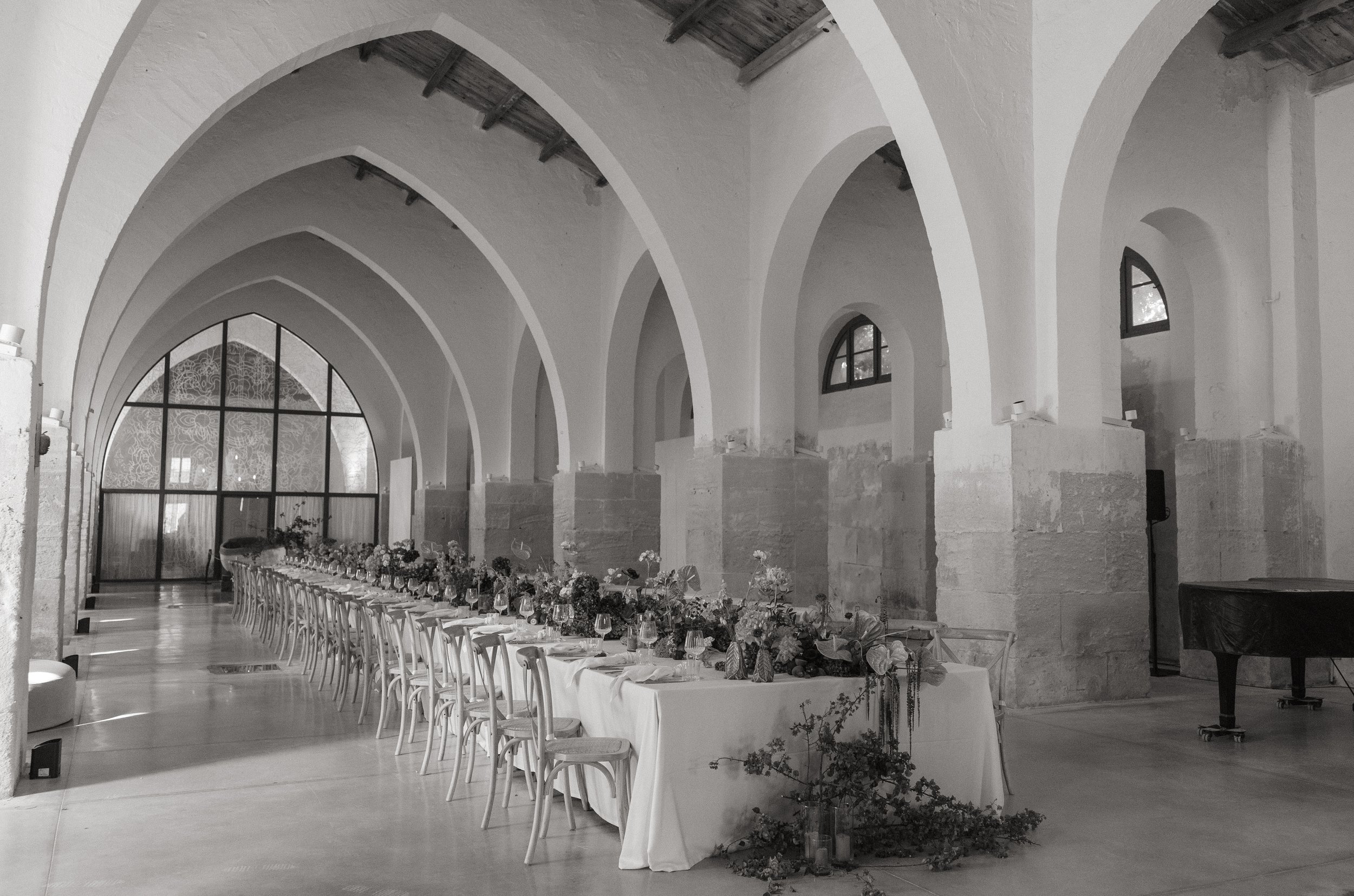 Editorial wedding photography of a long floral reception table beneath the historic vaulted arches of Camparia Favignana in Sicily.