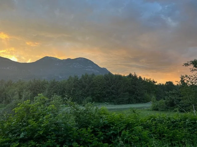 Sunset over a forested mountain landscape with a partly cloudy sky.