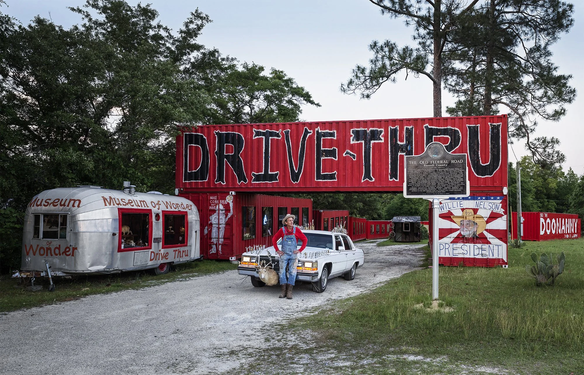 Butch Anthony at his Drive-Thru Museum of Wonder, standing in front of the 1989 Cadillac Fleetwood Brougham he obtained in a trade with singer/songwriter Leon Russell. Seale, Alabama. 2024.