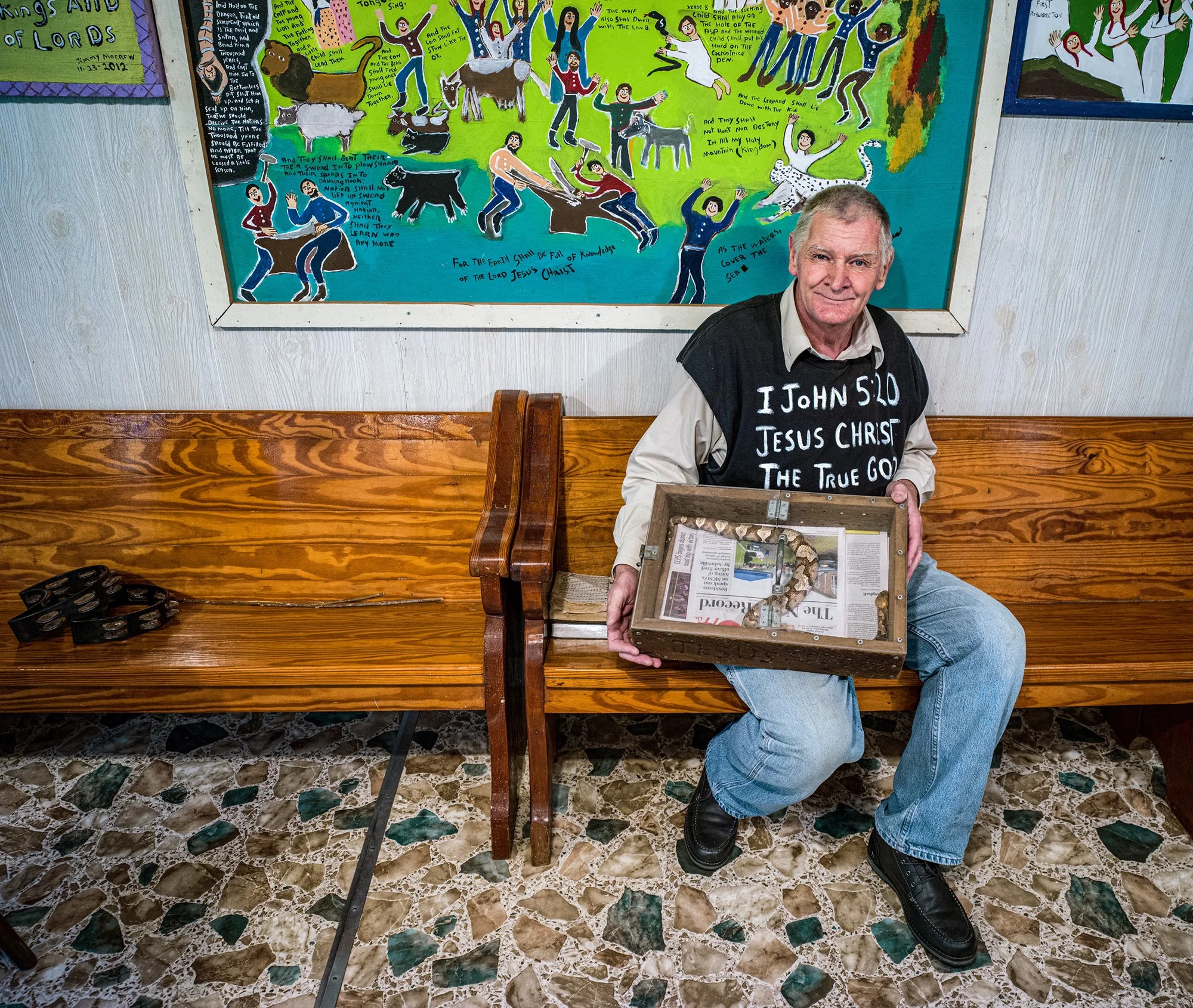 Reverend Jimmy Morrow in front of three of his paintings, holding an Eastern Timber Rattlesnake. Newport, Tennessee. 2021.