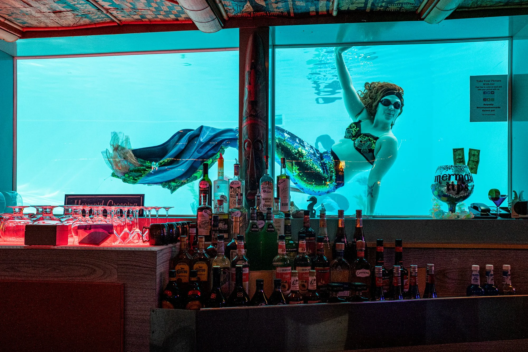 Mermaid in swimming pool, viewed through the Sip n' Dip Lounge. Great Falls, Montana. 2019.
