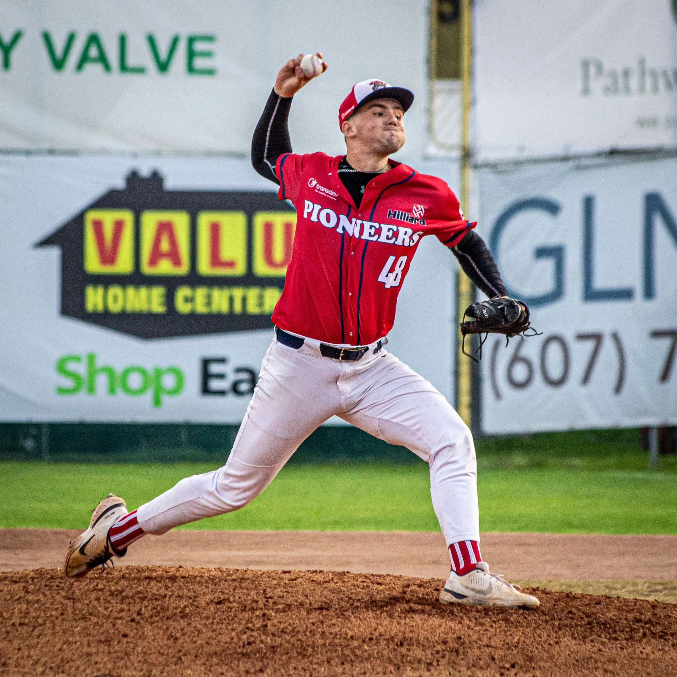 A baseball player in red and white uniform running on the field, holding a baseball in his right hand, wearing a cap, and white pants with red stripes.
