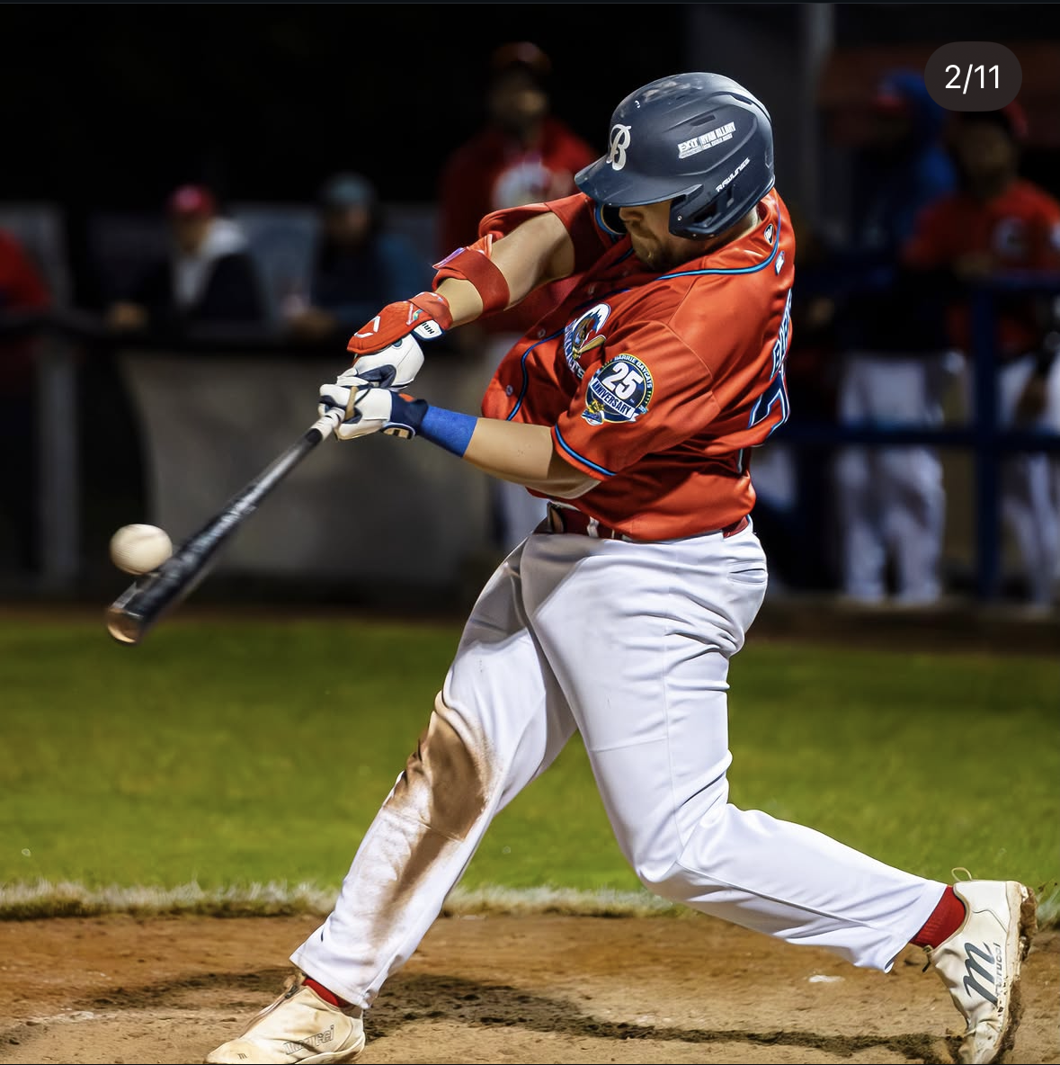 A baseball player in a red jersey and white pants swinging a bat at a pitch during a game.