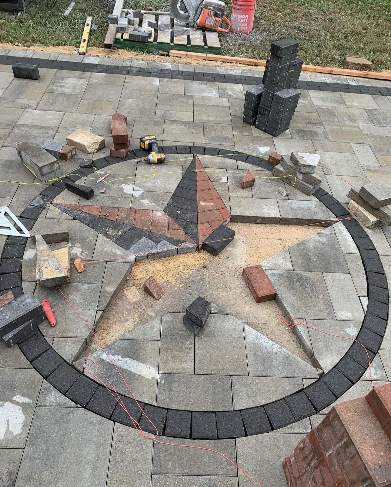 Stone patio with partially constructed star design, surrounded by bricks and tools