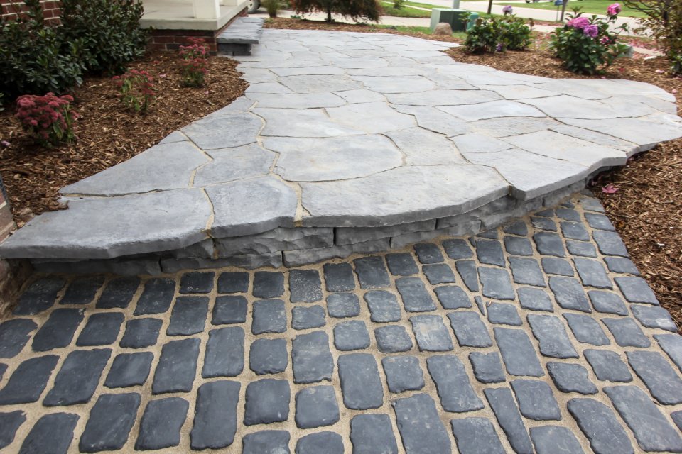 Stone pathway with cobblestone and flagstone sections in a landscaped garden setting with plants and mulch.