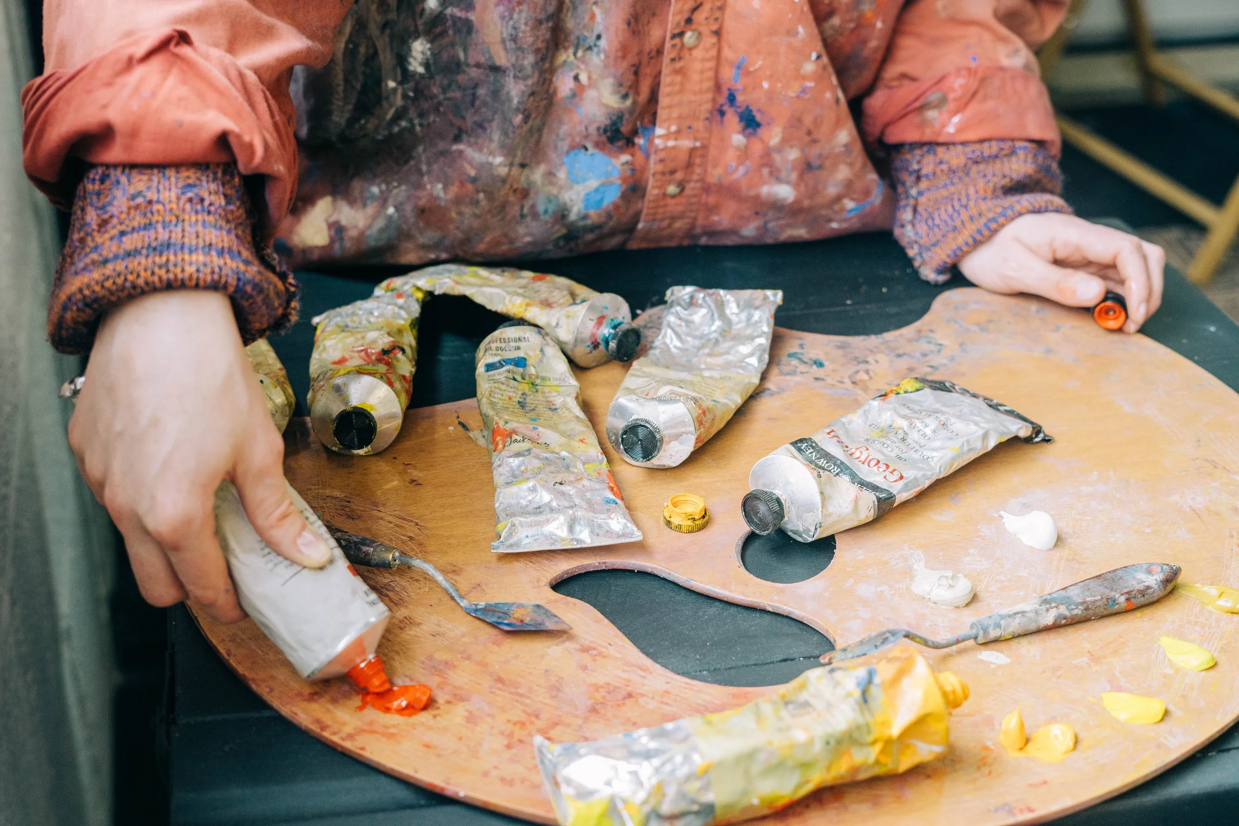 A photo of Genevieve's hand squeezing paint from a tube on a wooden palette