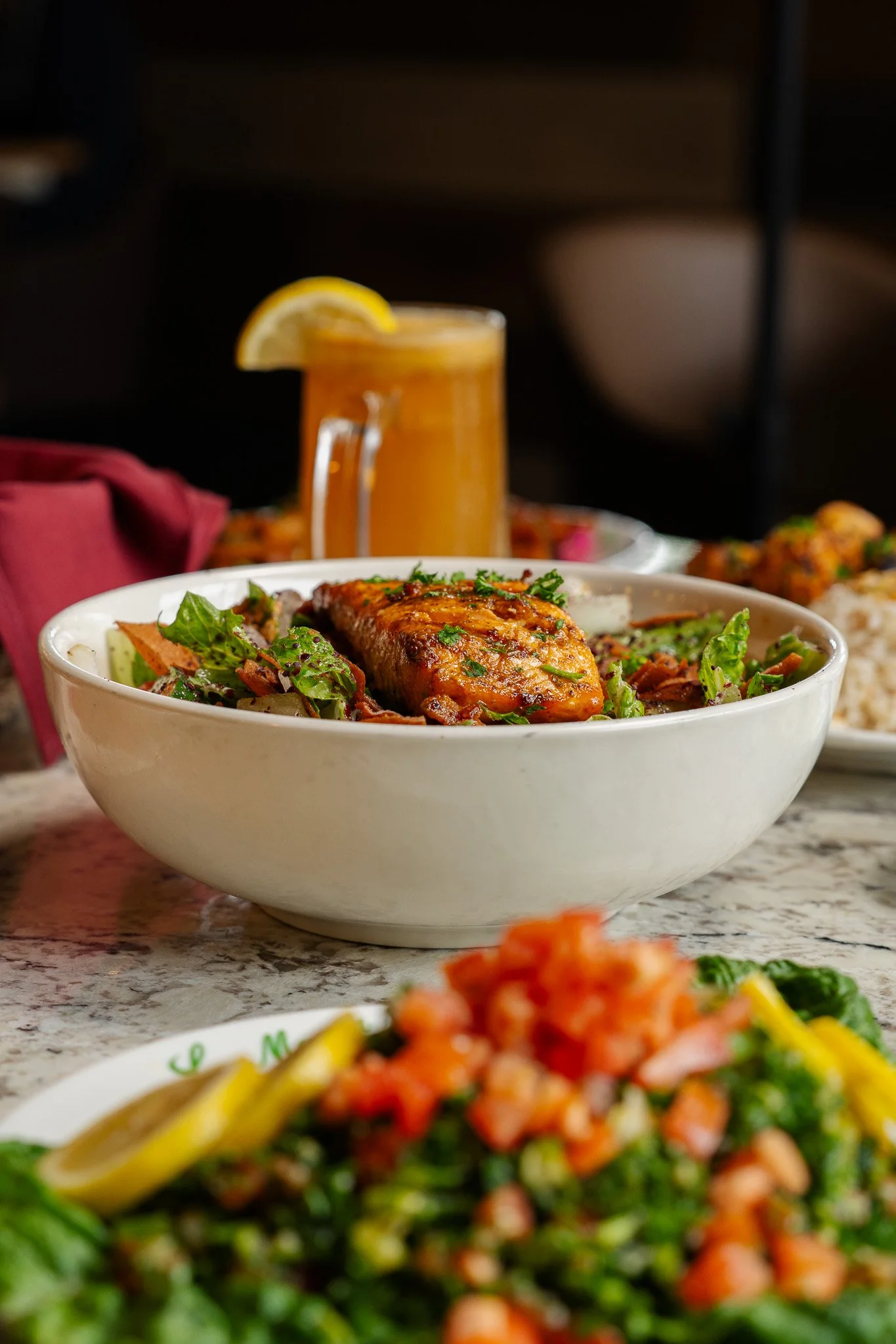 Close-up of a bowl with grilled salmon and salad alongside a glass of orange juice on a table with other dishes.