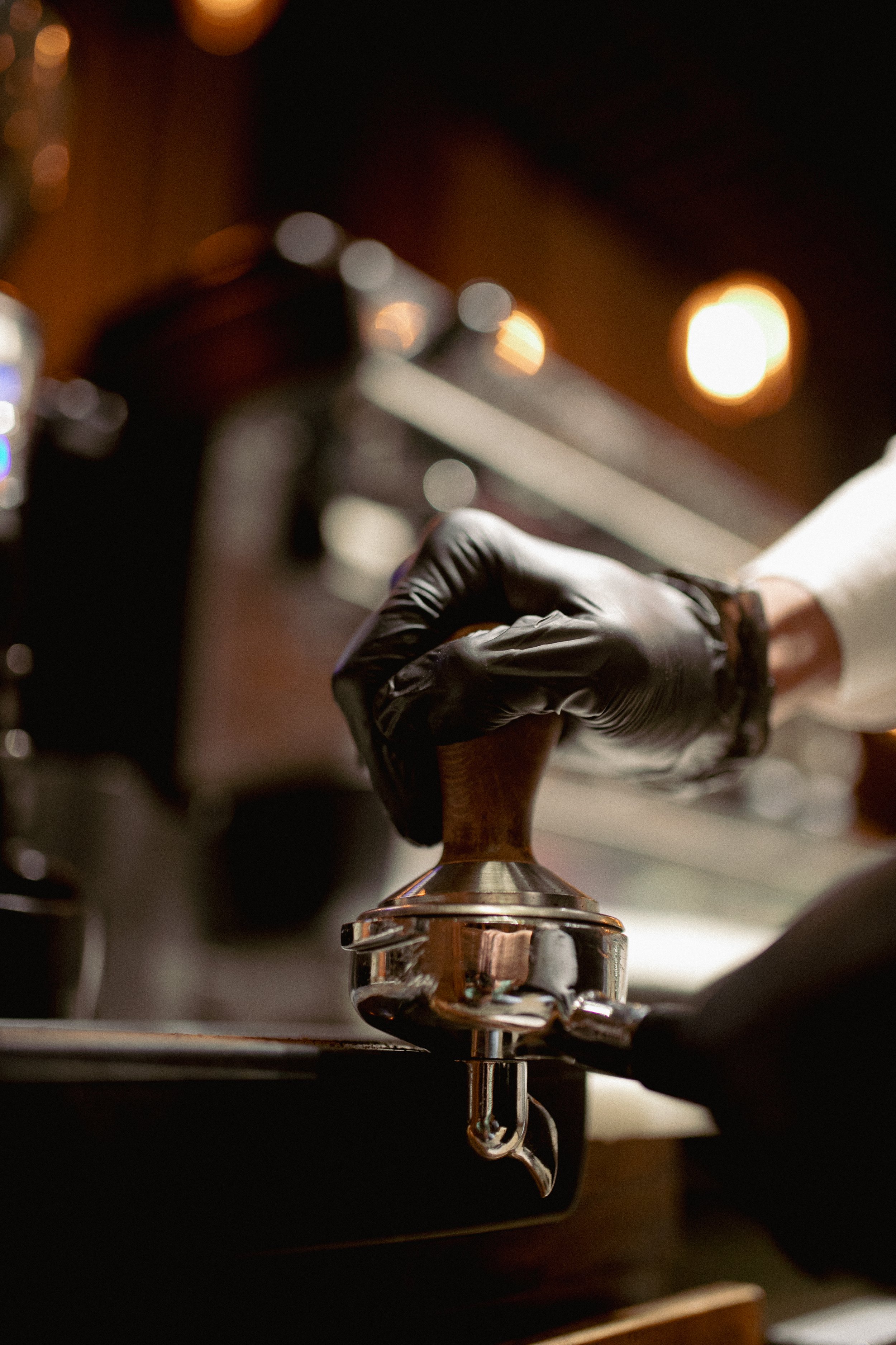 Barista tamping coffee grounds in portafilter with gloved hand