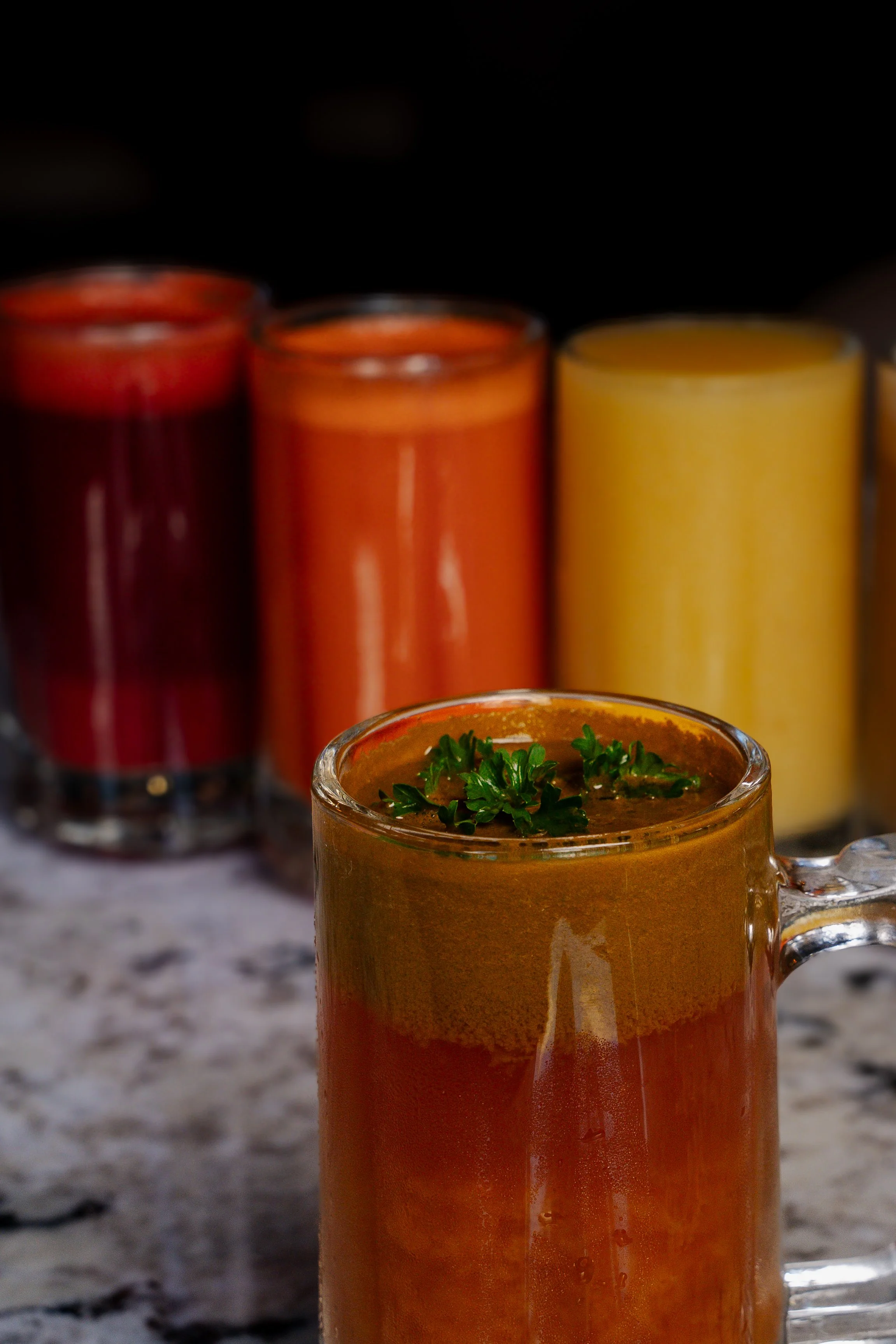 Various colorful fruit and vegetable juices in glass mugs on a marble surface.