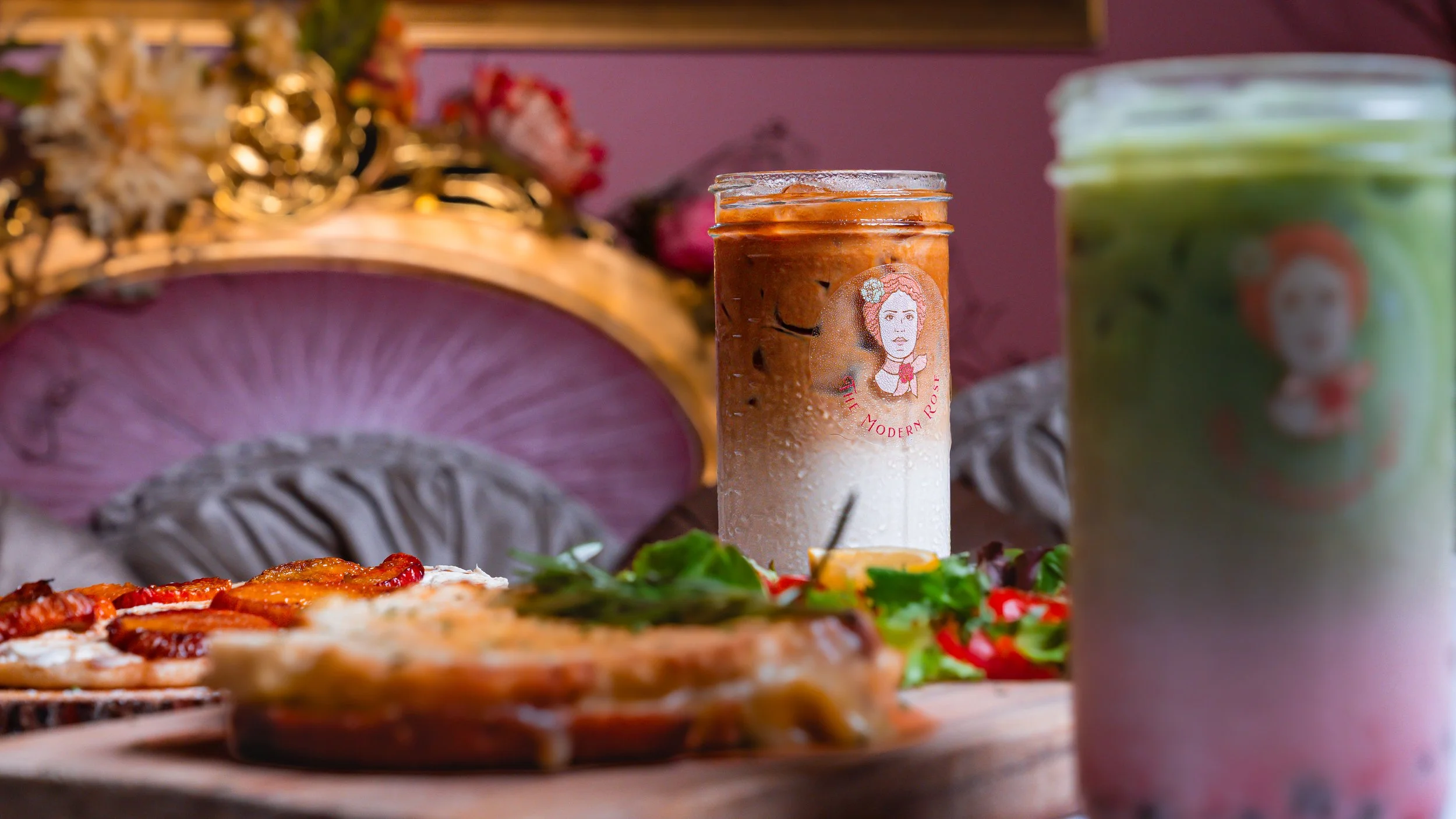 Iced coffee and matcha drinks in glasses with sandwiches and salad, floral background.
