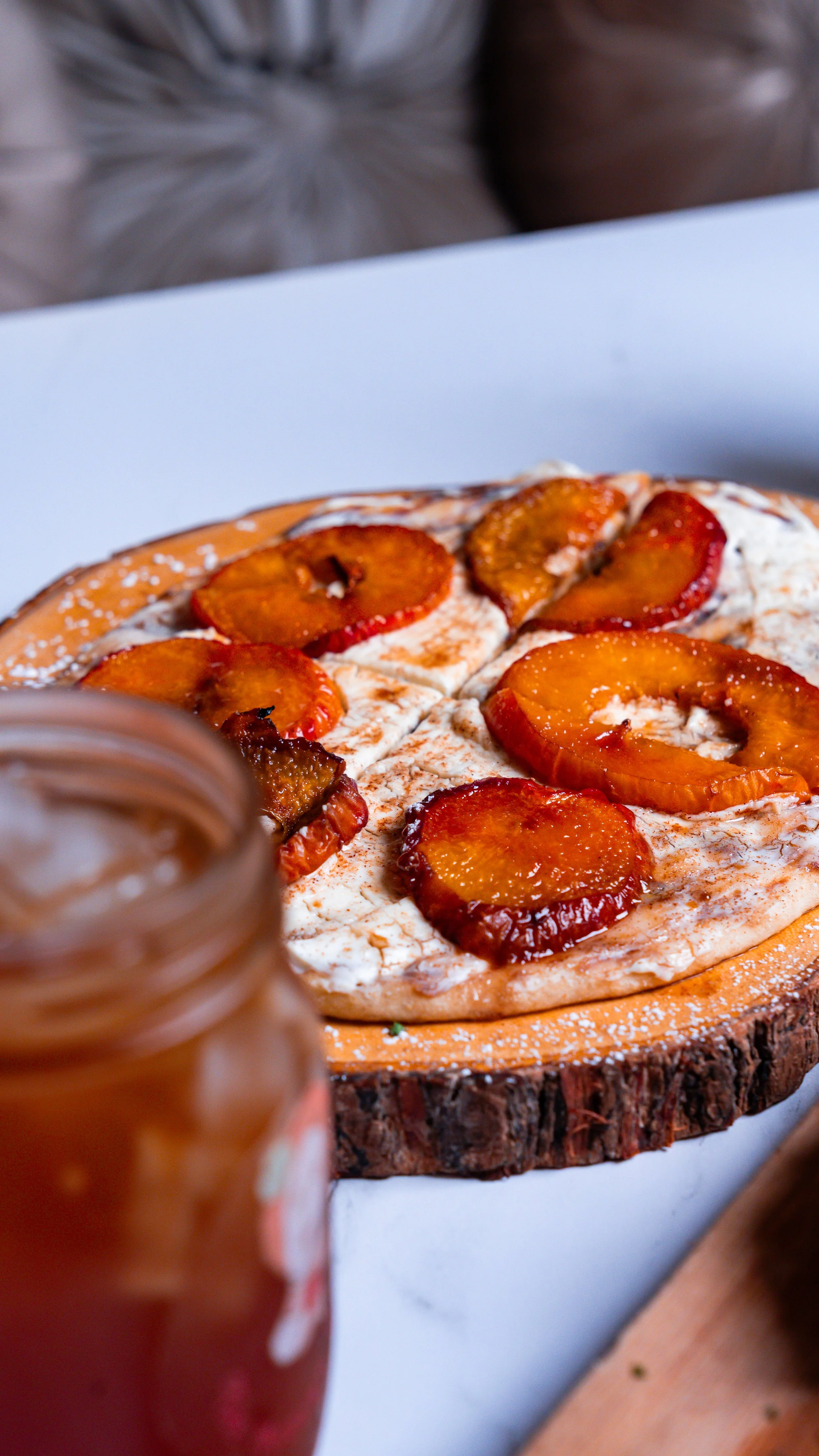 Pizza with fruit and cream on wooden board, jar of sauce in foreground.