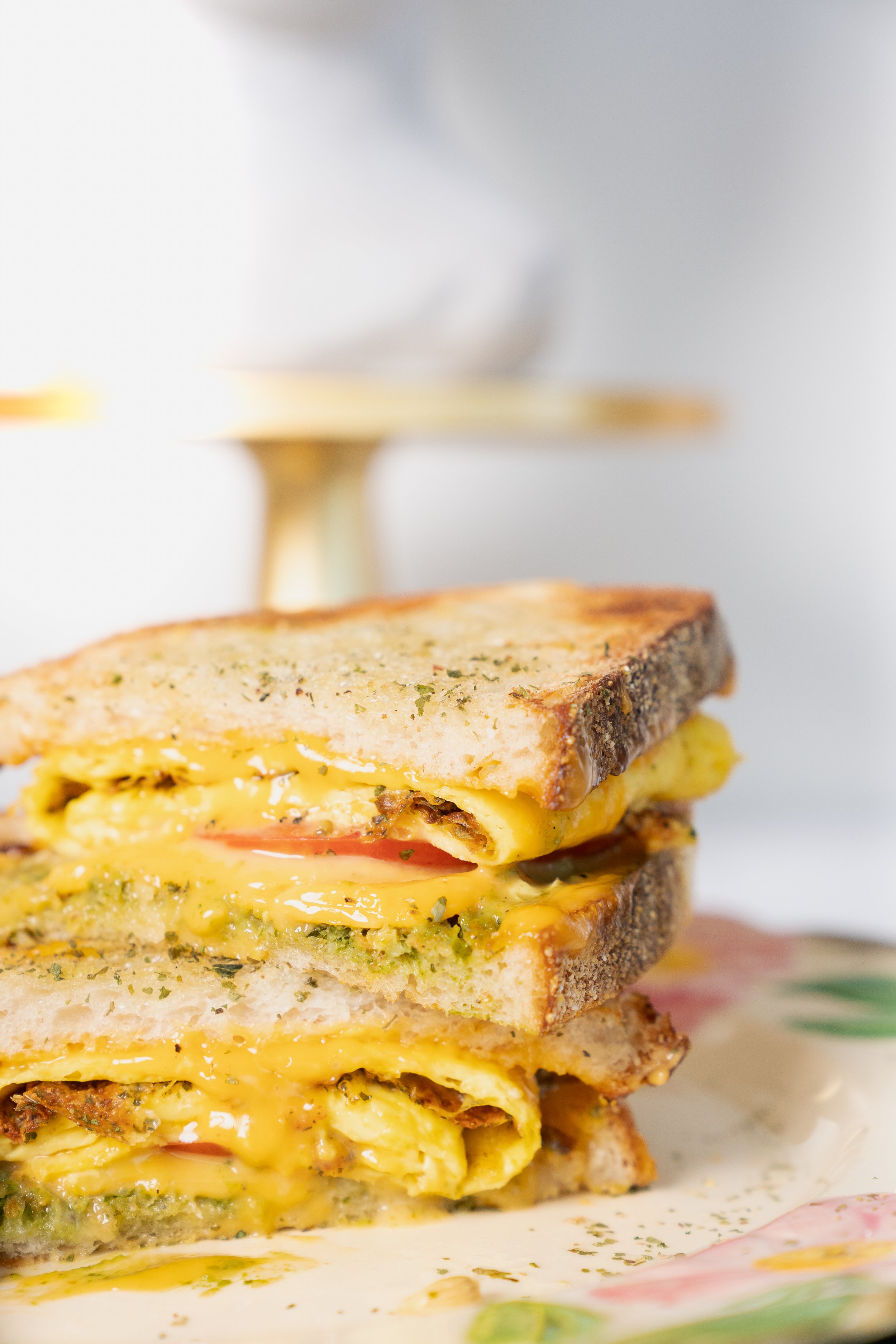 Close-up of a grilled cheese sandwich with melted cheese and herbs on rustic bread, sliced in half on a floral plate.