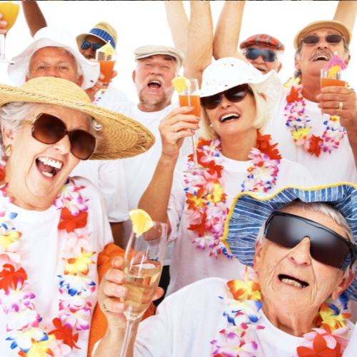 Group of elderly people celebrating with drinks, wearing sunglasses, leis, and hats, smiling and posing for a festive gathering.