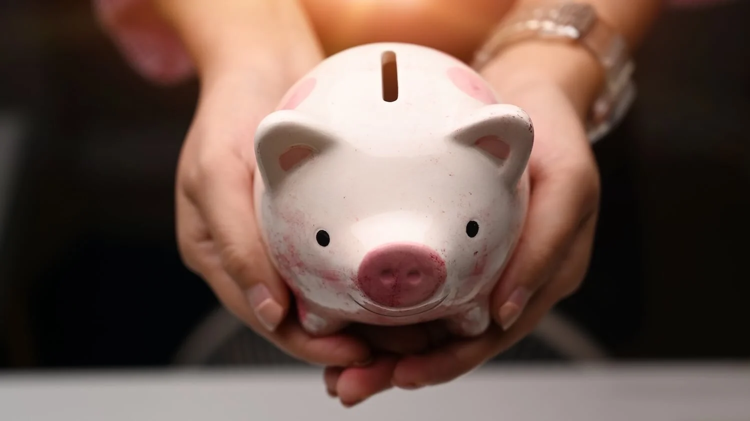 Close-up of a person holding a white and pink piggy bank, symbolizing charitable donations and financial support for community causes.