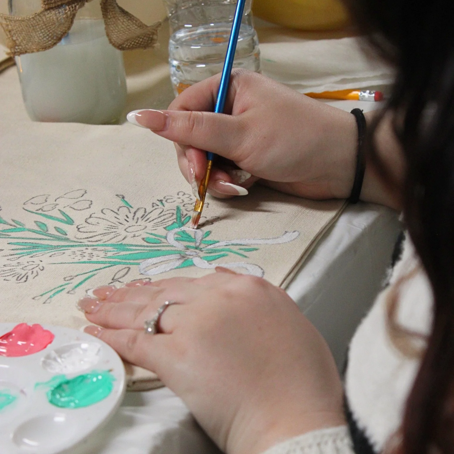 Person painting floral design on fabric during a guided art activity connected to Creative Roots art programming.