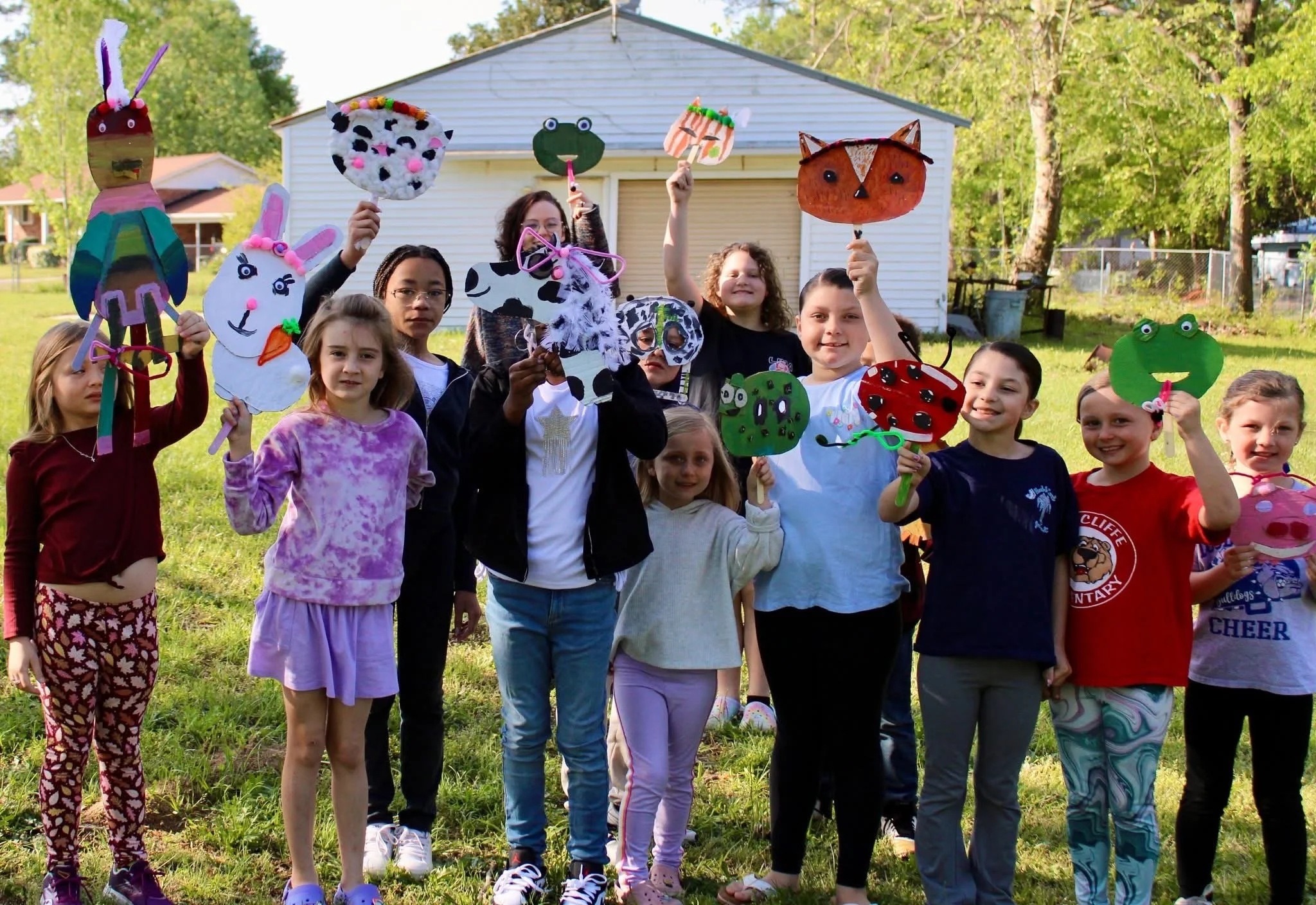 Children participating in an outdoor art activity, holding handmade paper puppets during a children's art class in Beech Island, South Carolina.