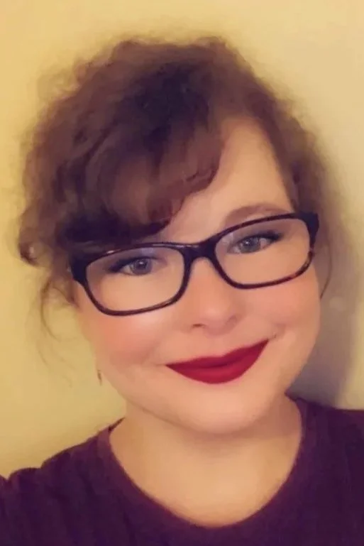 Britney Hardin, Arkansas Counselor, MBA, LAC, LAMFT, with curly hair, wearing black glasses and red lipstick, smiling at the camera.