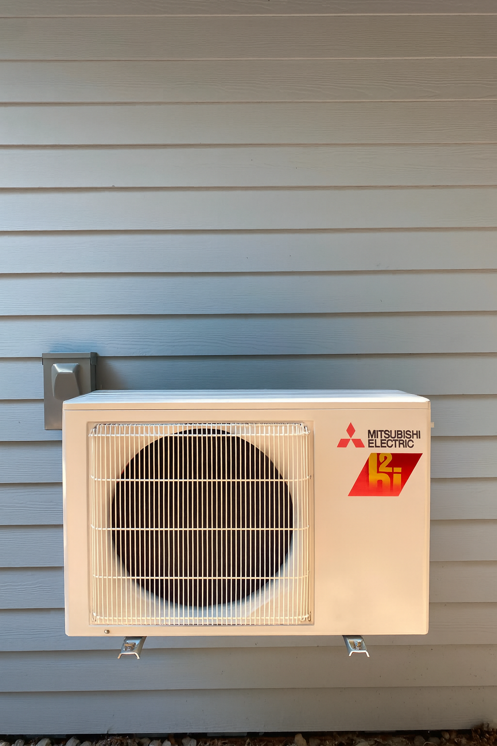 Exterior Mitsubishi Electric HVAC unit mounted on light blue horizontal siding wall.