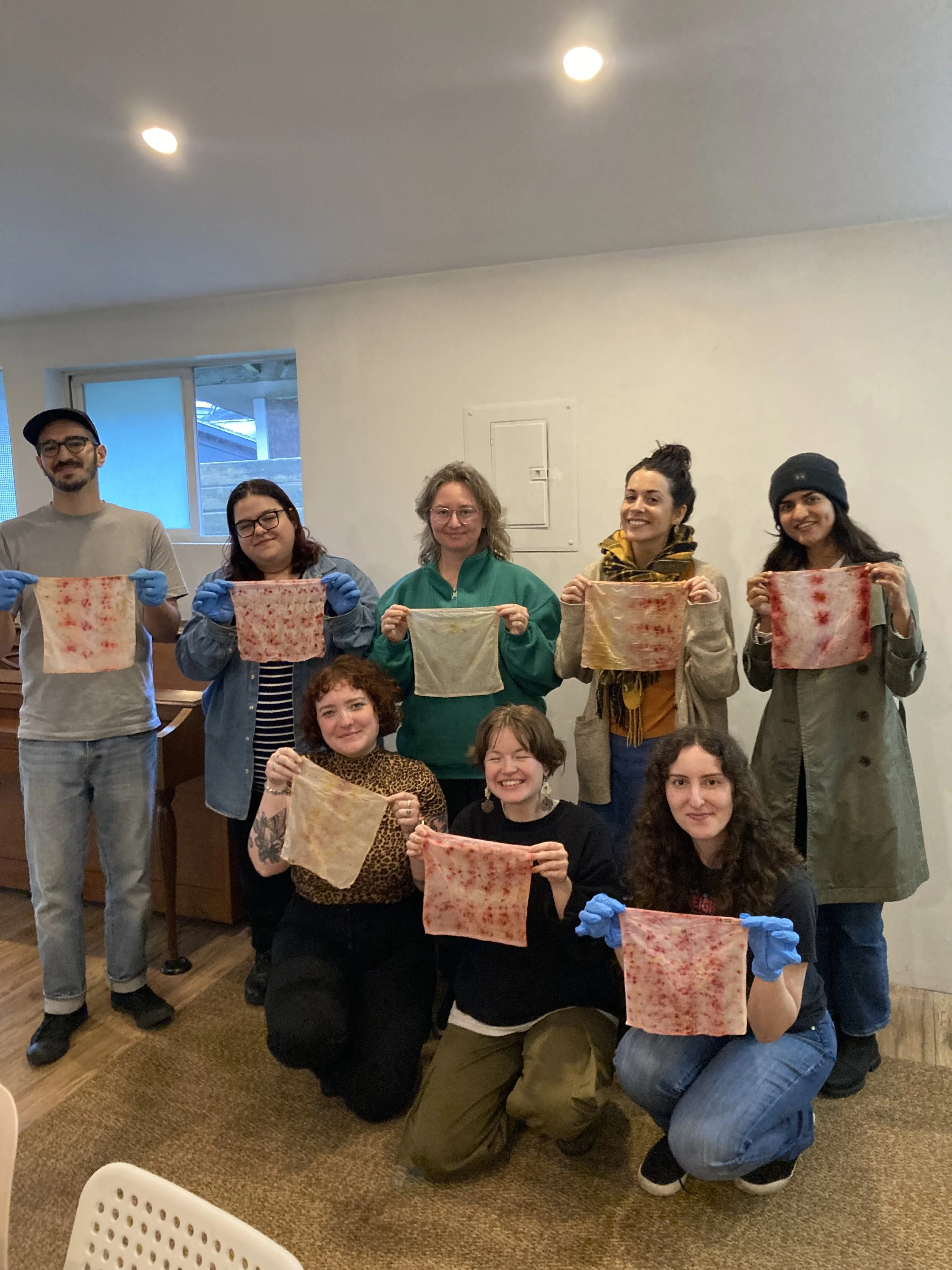 Participants smiling and holding up their eco-printed fabric during an indoor eco-art team-building workshop led by Alexandria Thompson in East Vancouver