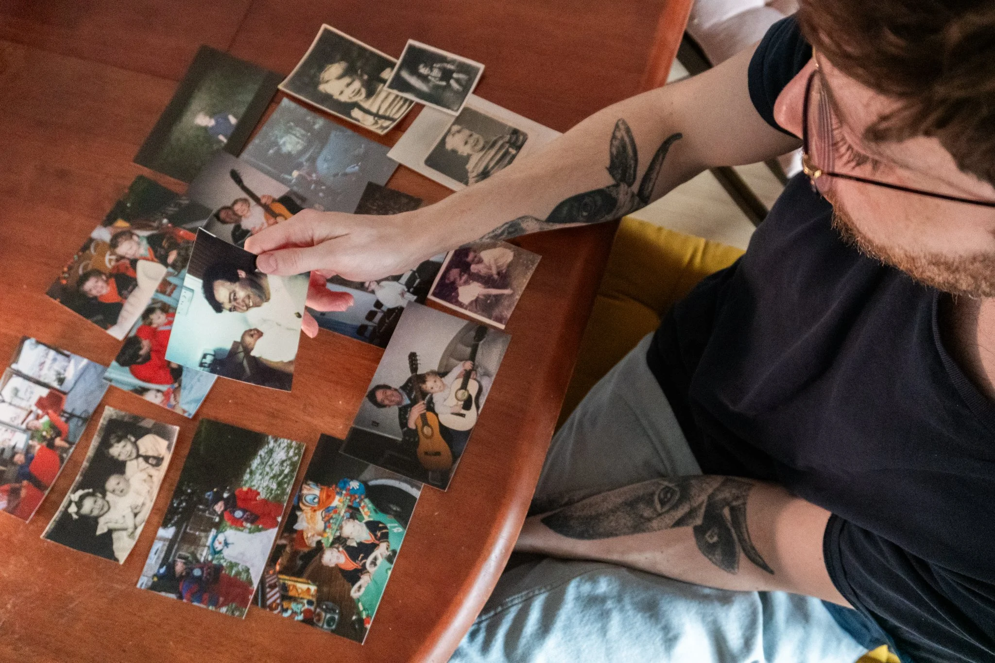 Jack is sitting at a table, holding a photograph of him as a baby with his dad. There are more of his old photographs on the table.