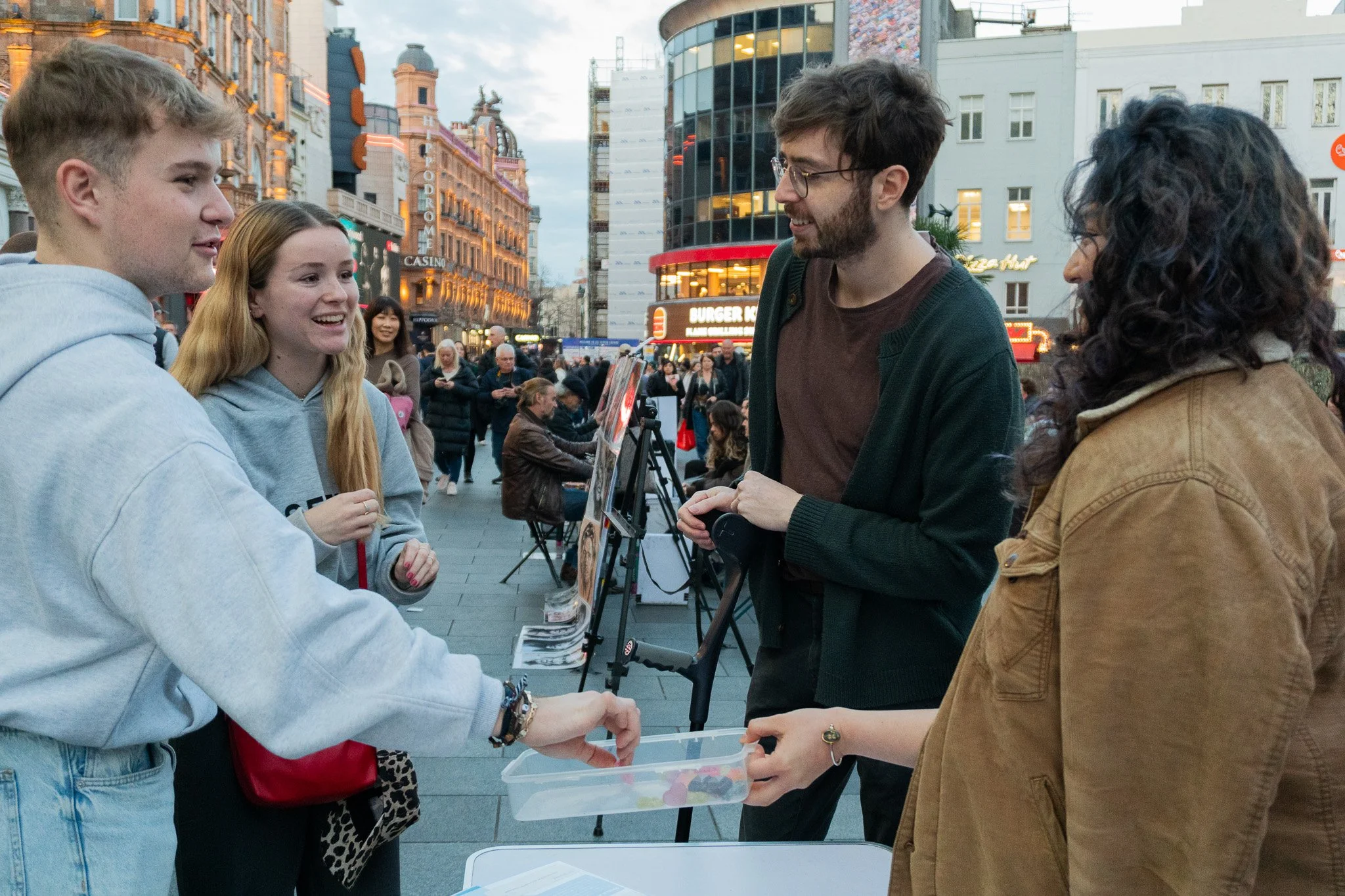 Jack is talking to two passersby, who are smiling and taking vegan candy from another activist next to Jack.