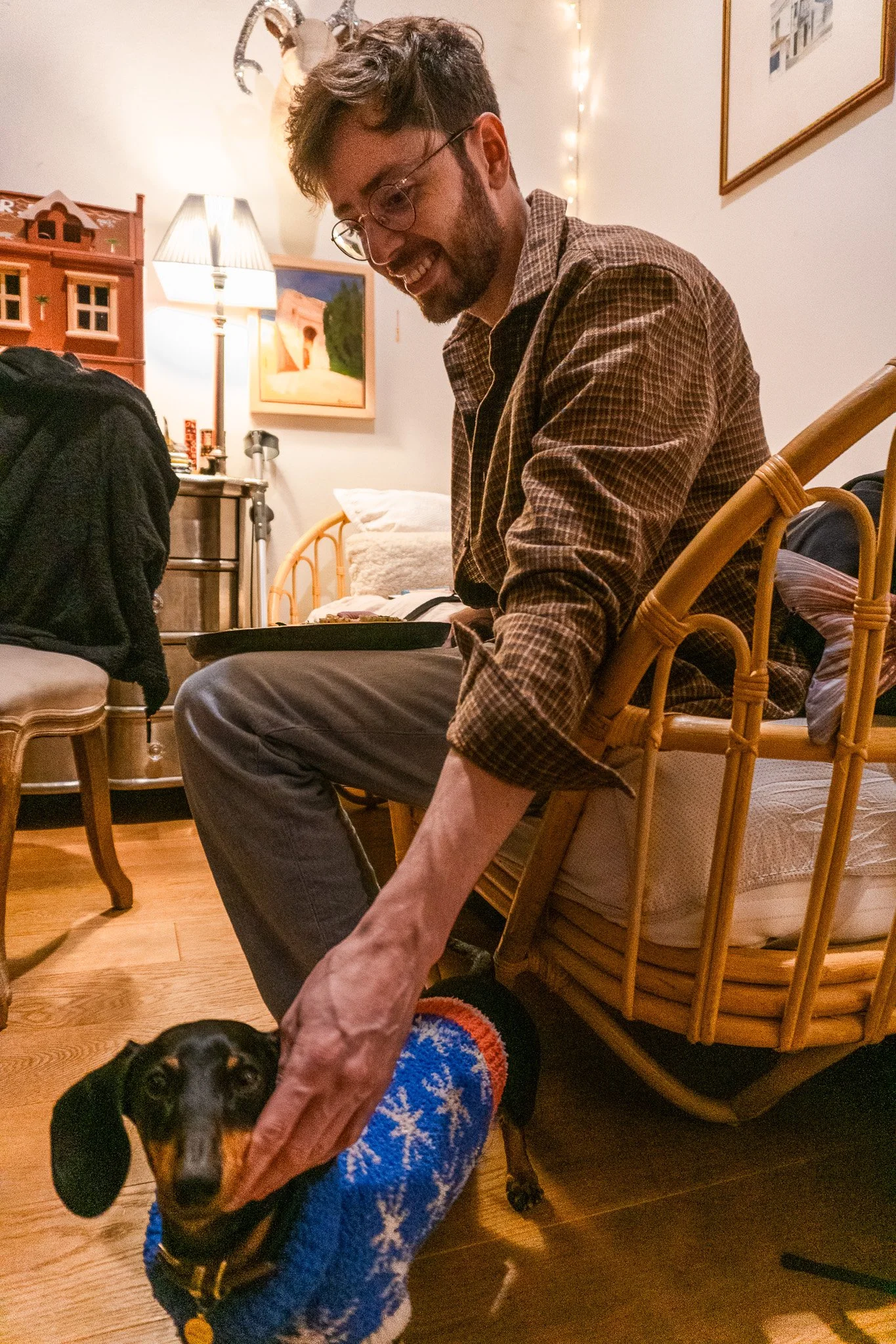 Jack is sitting on a couch. He is smiling and extending his arm to pet a small dog.