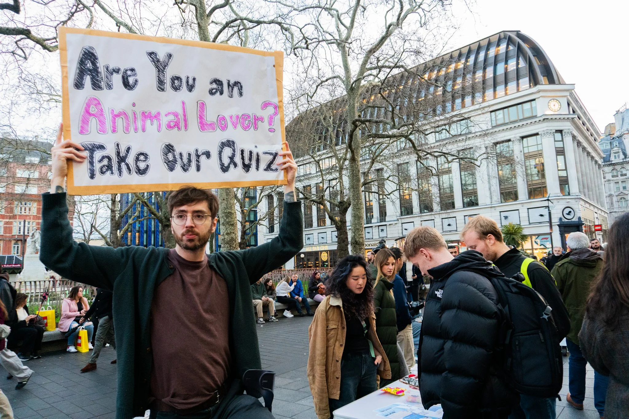 Jack is holding a sign "Are you an Animal Lover? Take a Quiz" above his head at a Leicester Square in London.