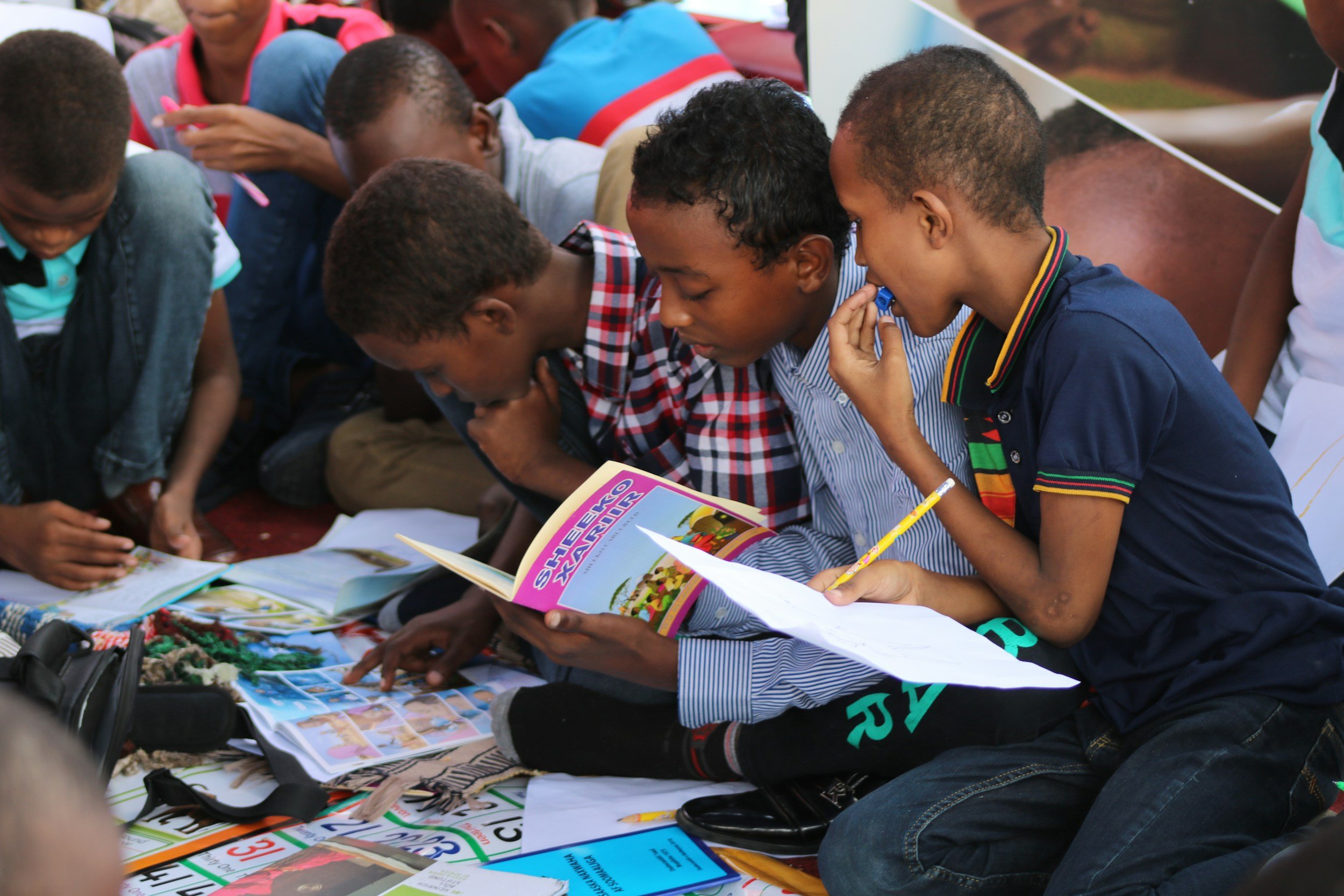 A group of young boys sitting small group learning and collaboration time with peers, with some of them holding papers and pens, appearing engaged and focused.
