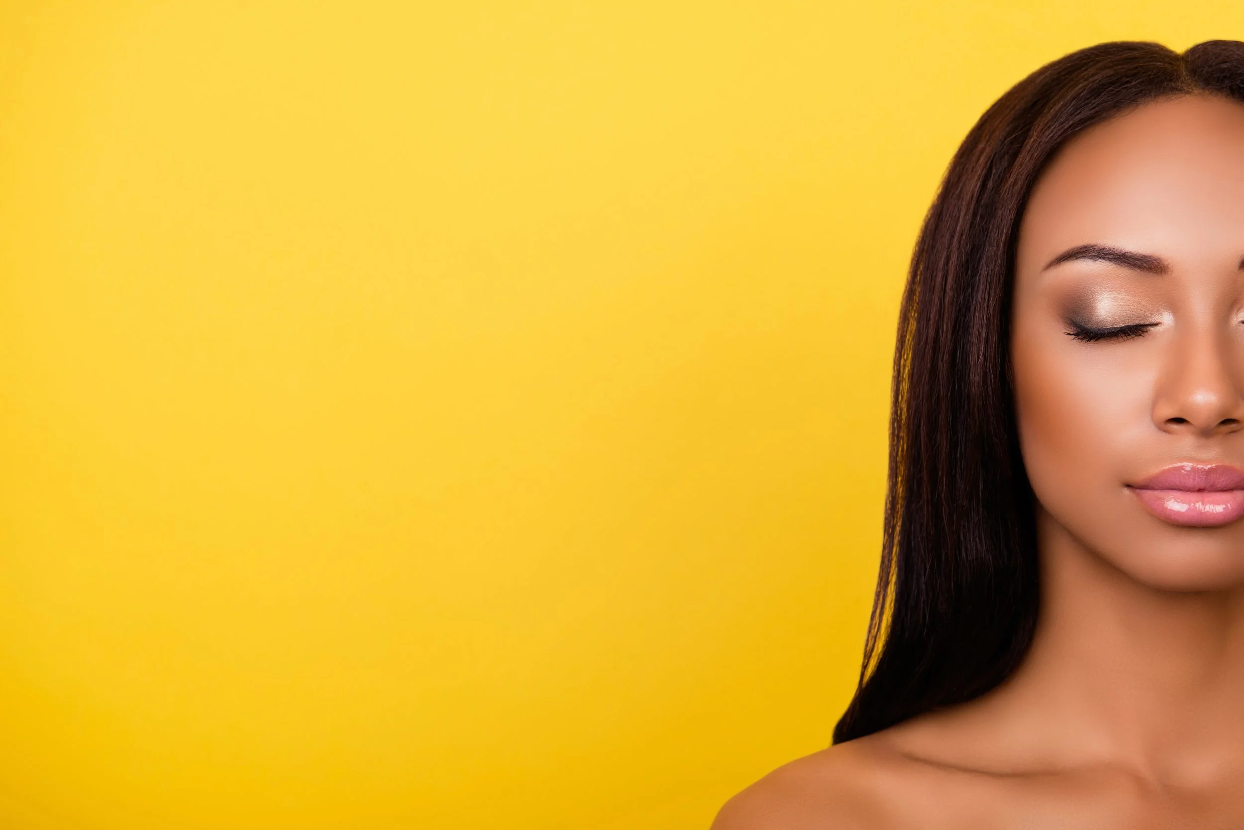 Close-up of a woman with closed eyes and long dark hair against a yellow background.