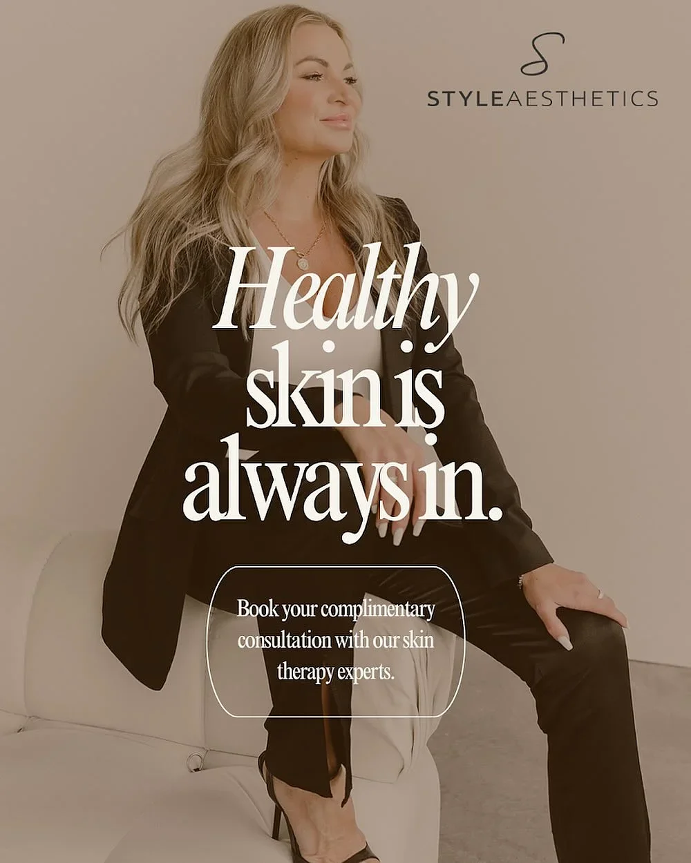 A woman with long blonde hair sitting on a white sofa, wearing a black blazer and pants, promoting skin health and an offer for a complimentary skin consultation by Style Aesthetics.
