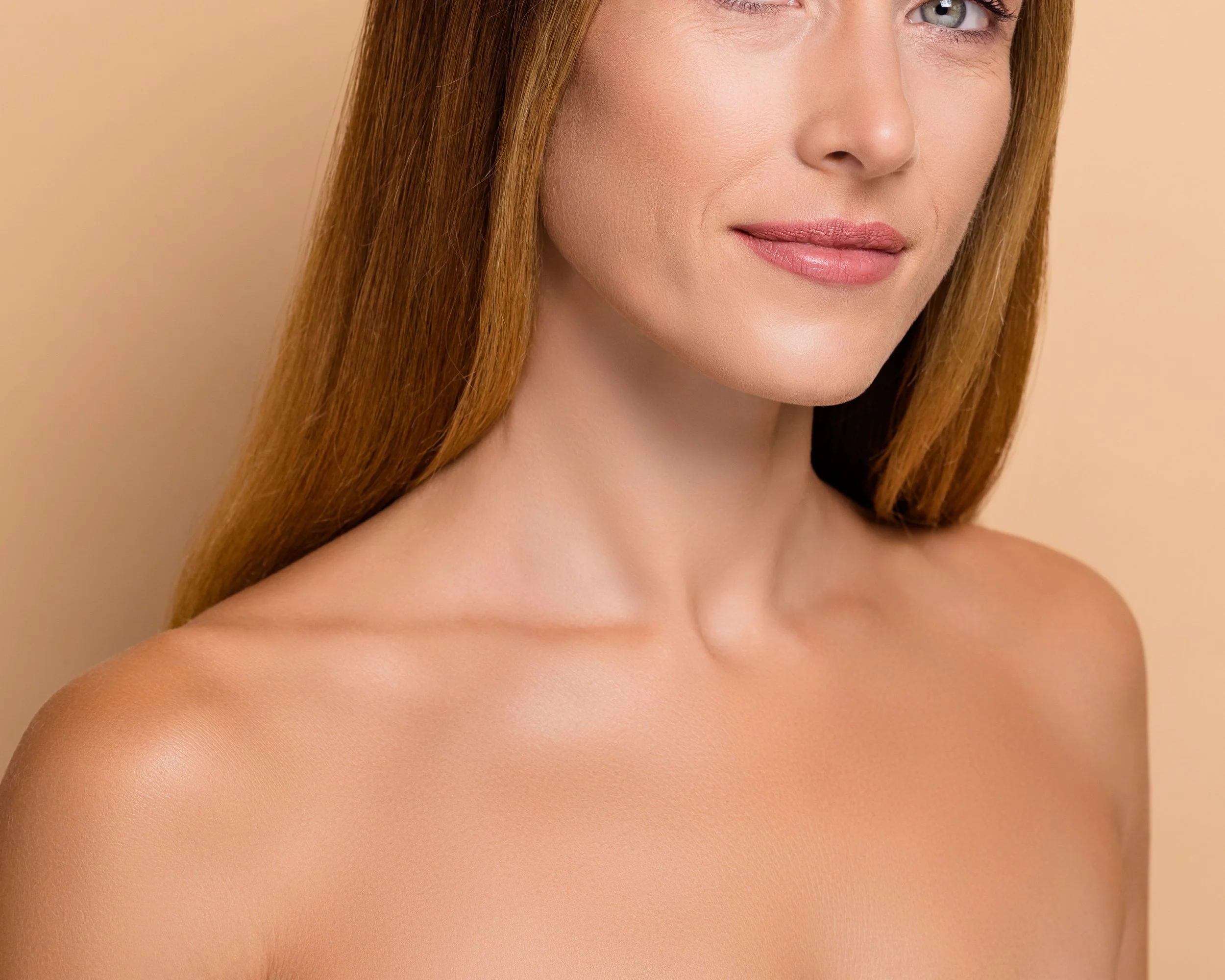 Close-up of a woman with fair skin and long red hair, showing her shoulder and part of her face, with a neutral beige background.