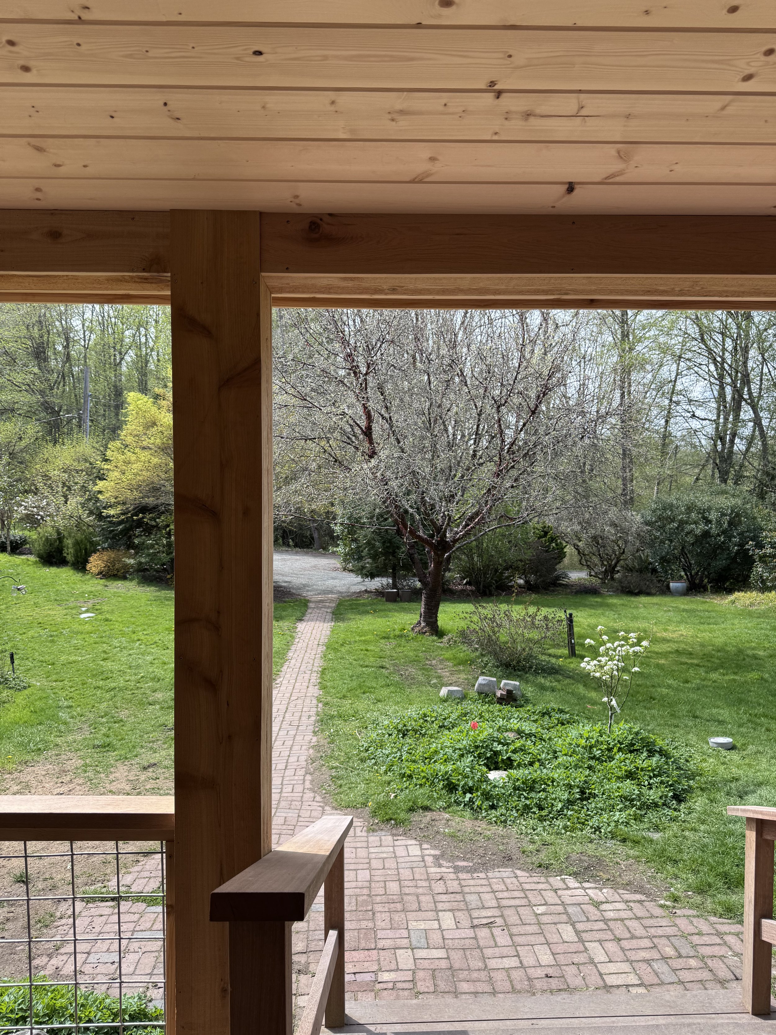 View from a porch showing a garden with trees, bushes, a brick pathway, and a grassy lawn.