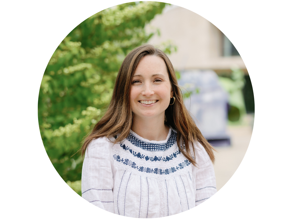 Woman smiling outdoors in a garden setting, wearing a striped sleeveless top with ruffled shoulders.