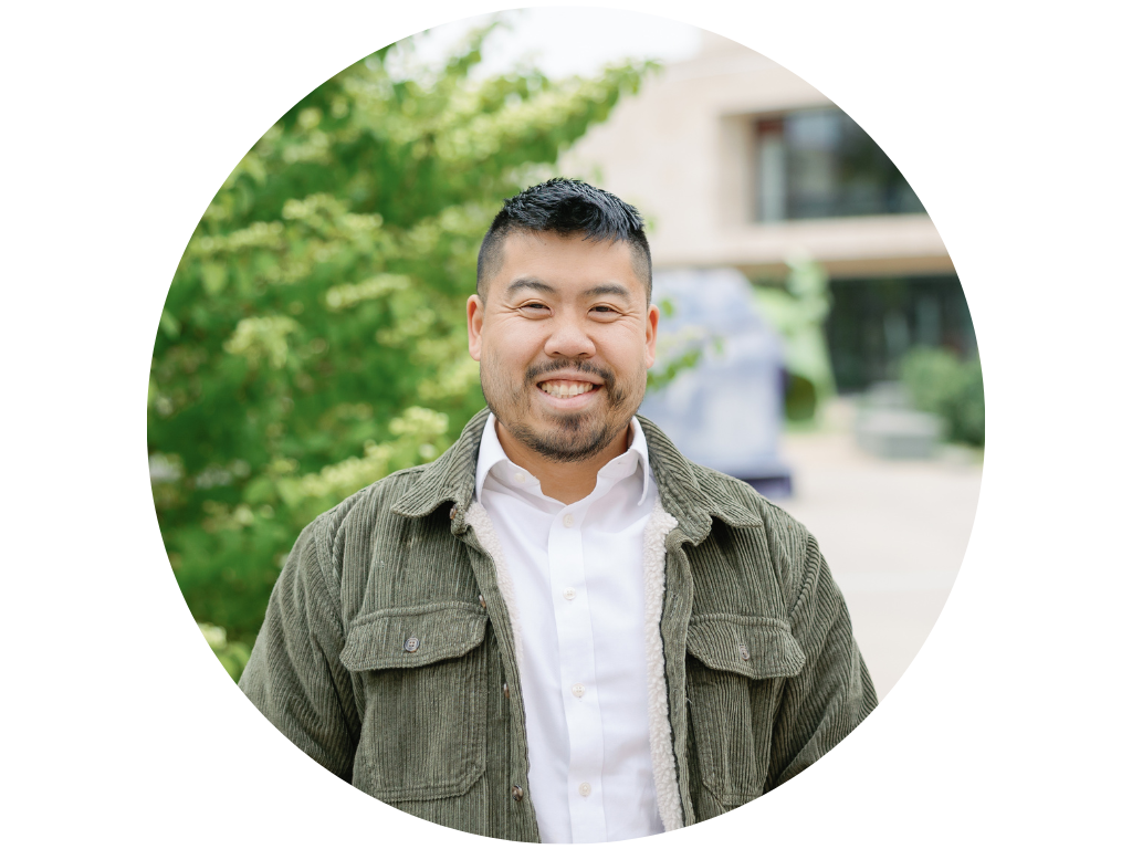 Person wearing glasses and a white shirt smiling outdoors with trees and greenery in the background.