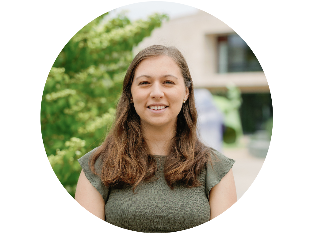 Person with shoulder-length brown hair and wearing a light blue sweater, standing in front of a wooden door.