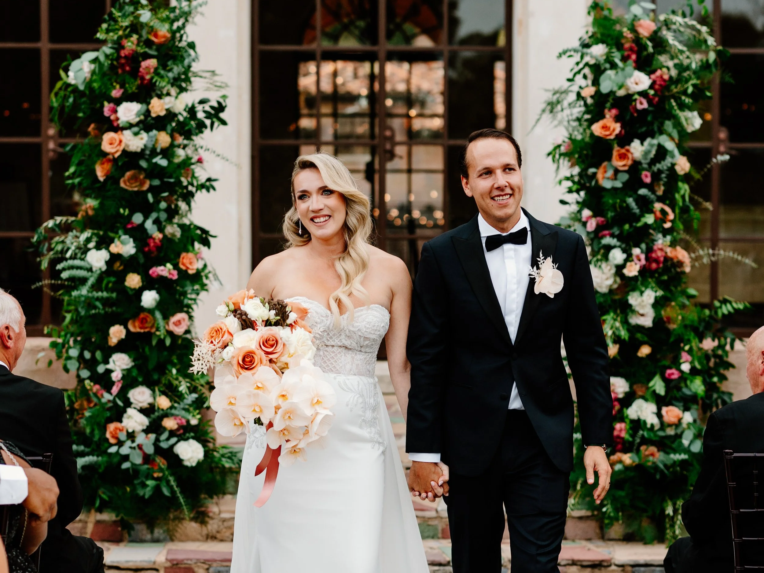 Emerald Gardenia bride and groom walking down aisle surrounded by wedding florals.