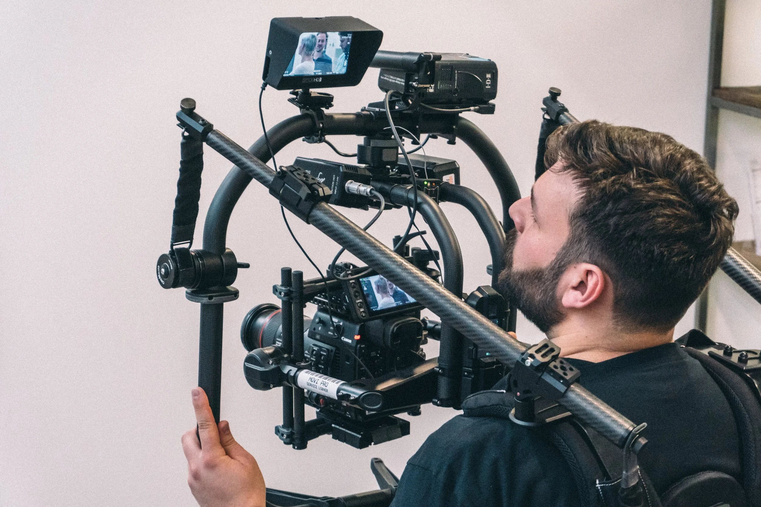 Landed Media, Videographer operating a professional cinema camera mounted on a stabilizer rig, filming a scene involving a woman and a man, both visible on the camera's screen.
