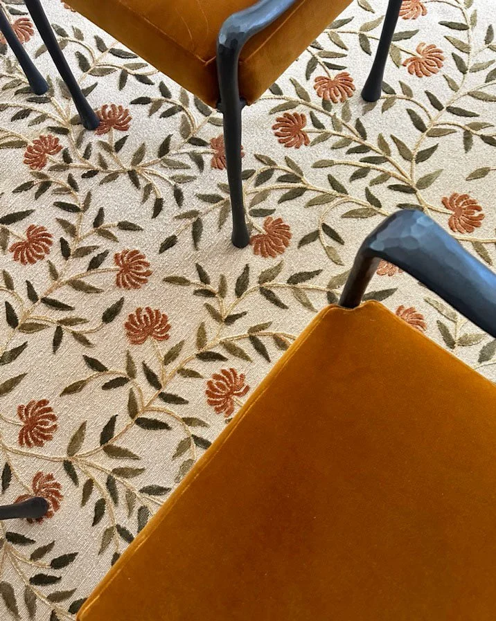 Close-up of copper velvet Gia chairs on a silk floral-patterned carpet with leaves and orange flowers.