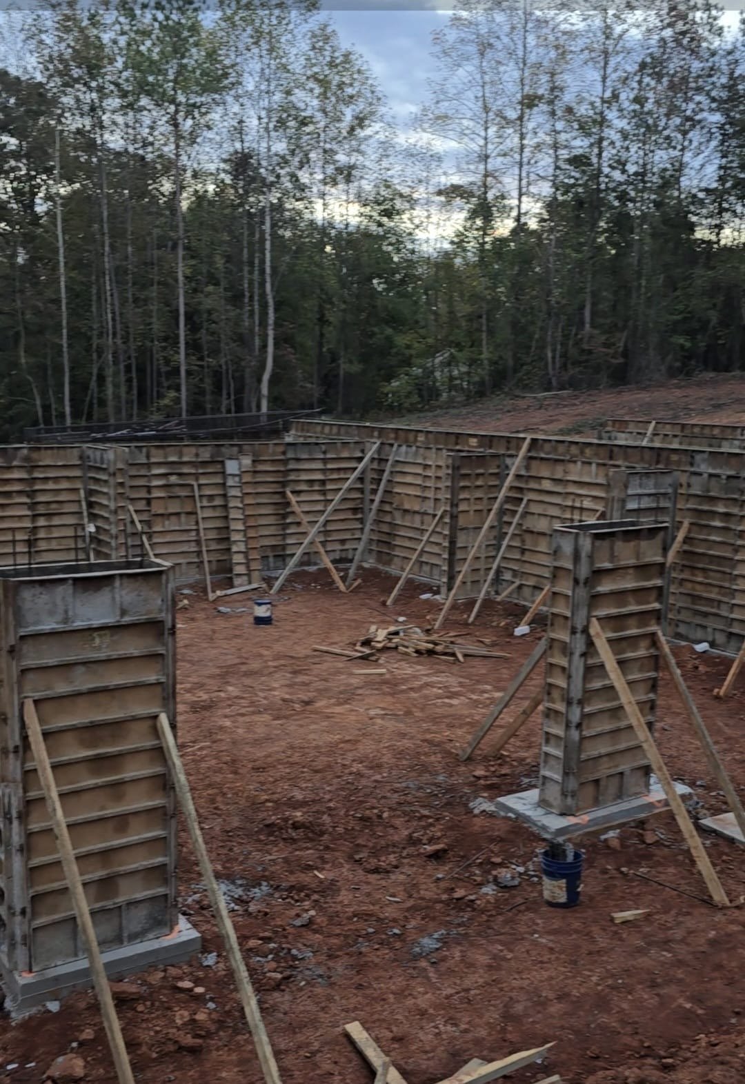 Wooden forms and supports for concrete foundation walls at a construction site surrounded by trees.