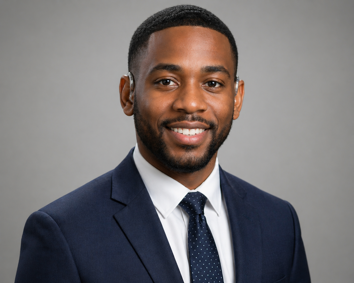 Black male with dark black short cut hair style with blue suit jacket, white shirt and blue tie, smiling.