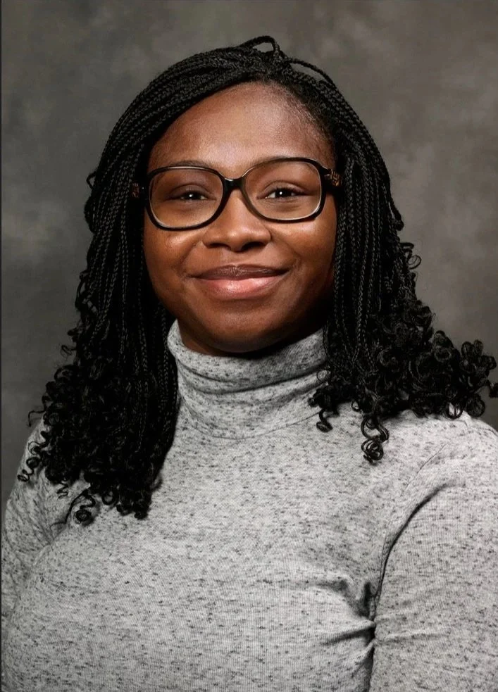 Woman with her hair down, wearing glasses and a gray shirt, smiling.