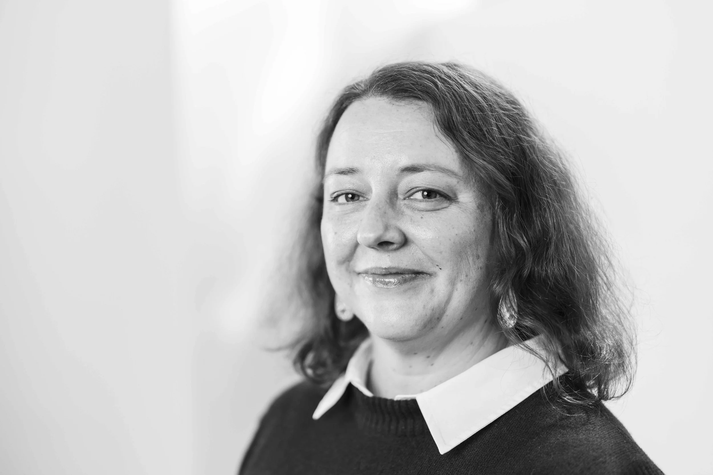 black and white image of woman aged 40 smiling with mouth closed wearing a plain shirt with knit