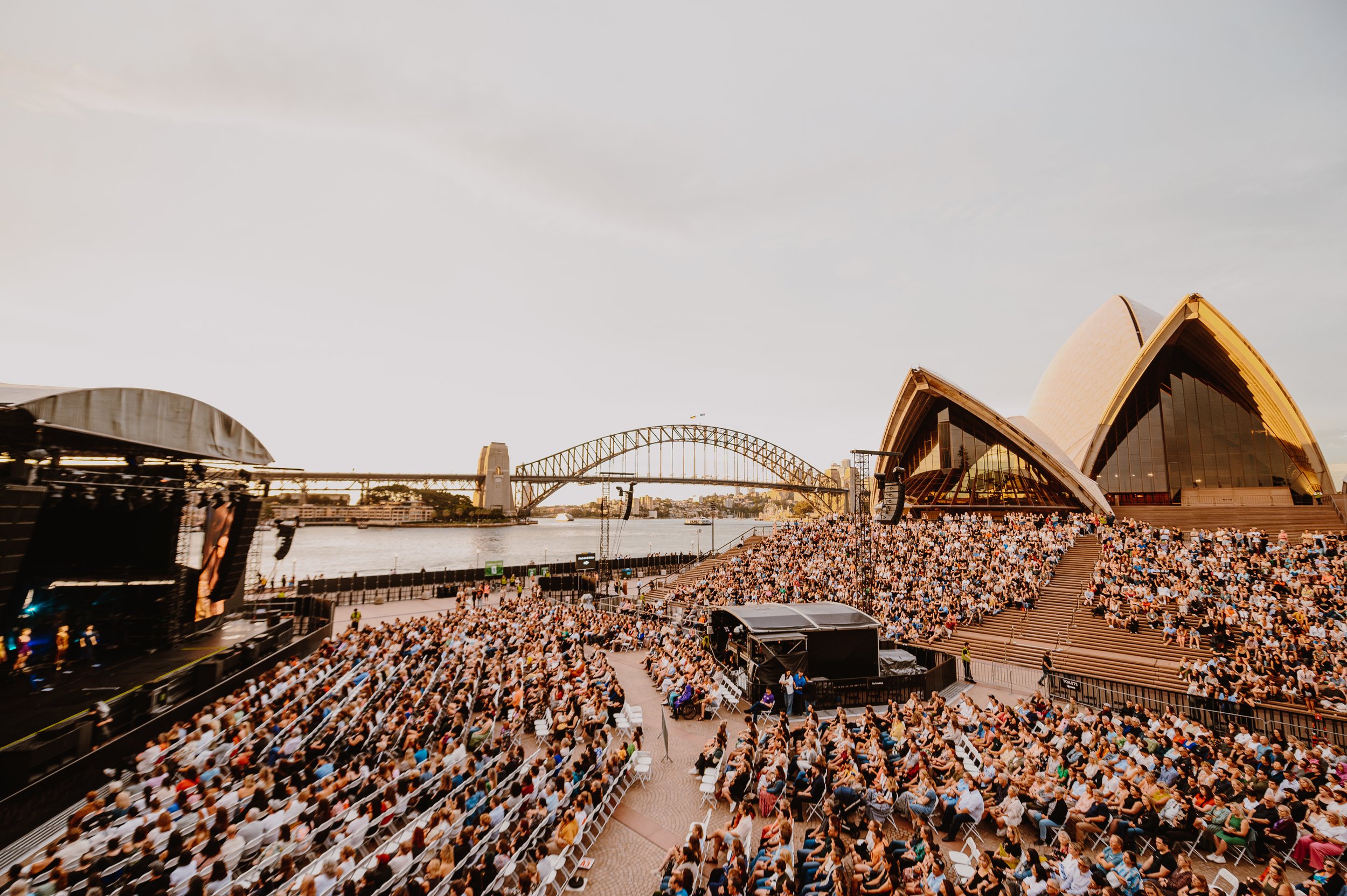 Crowd at outdoor concert near Sydney Opera House and Sydney Harbour Bridge during sunset