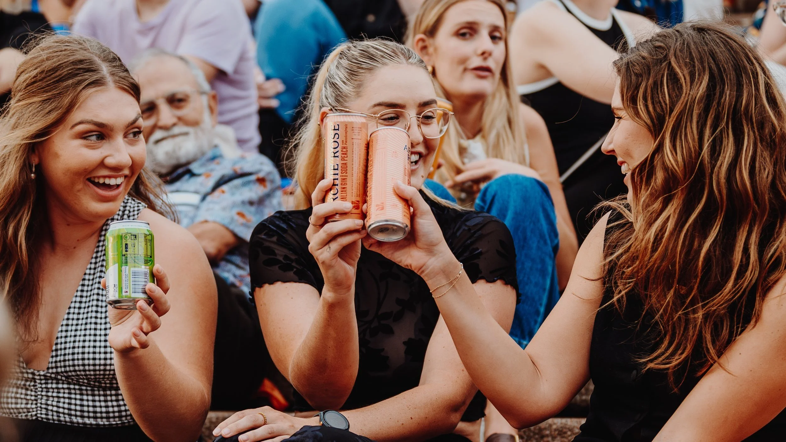 Girls cheersing their cans of Archie Rose drinks.