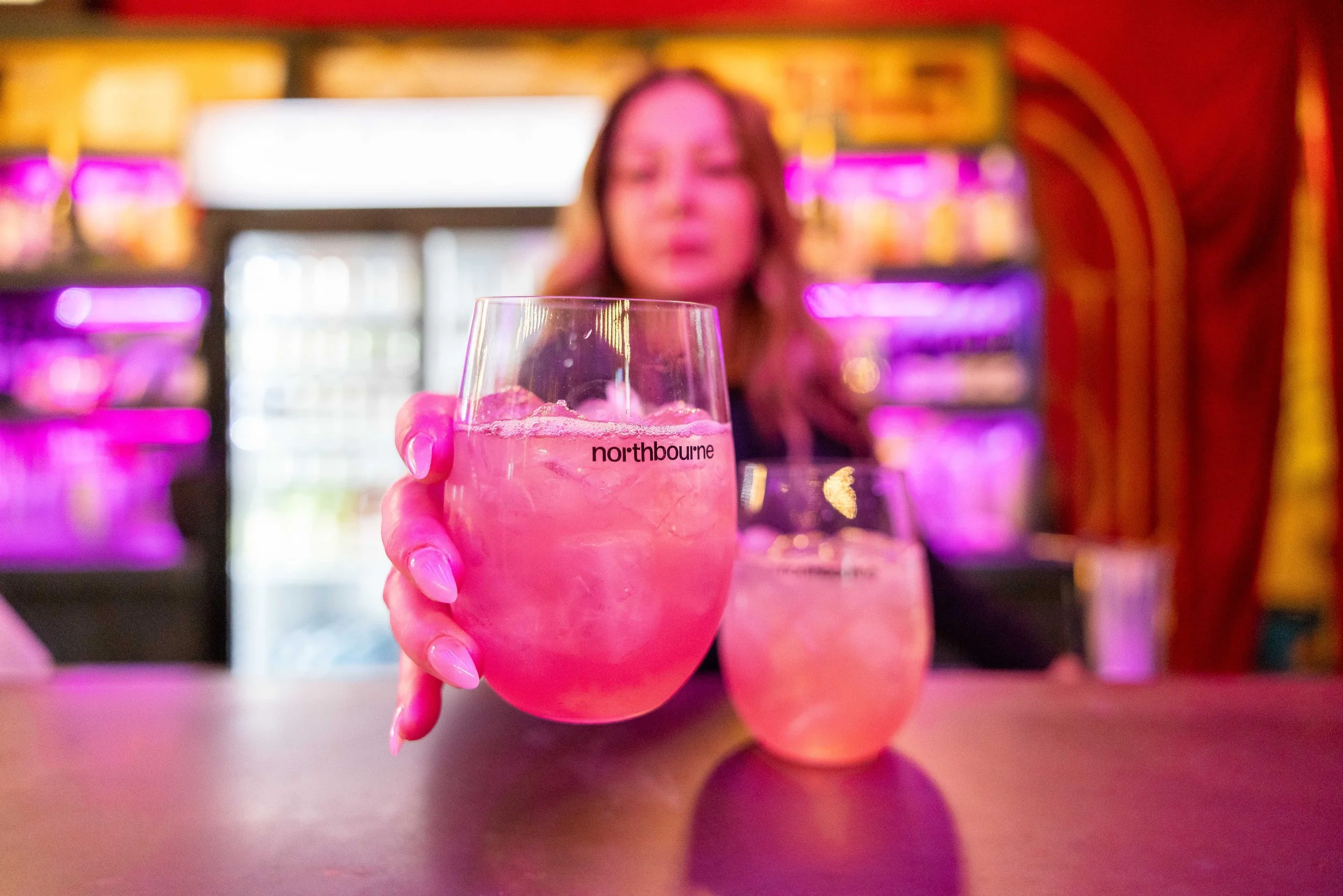 woman with long curly hair at bar setting glasses with Northbourne branding on bar