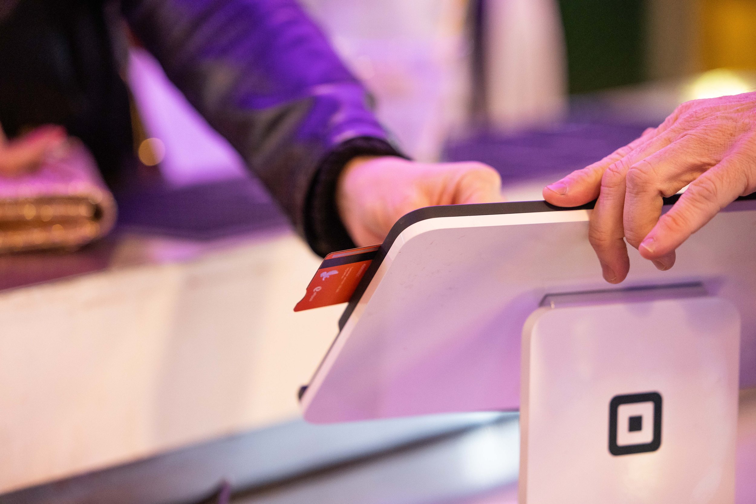 a hand using a credit card to tap on a Square POS