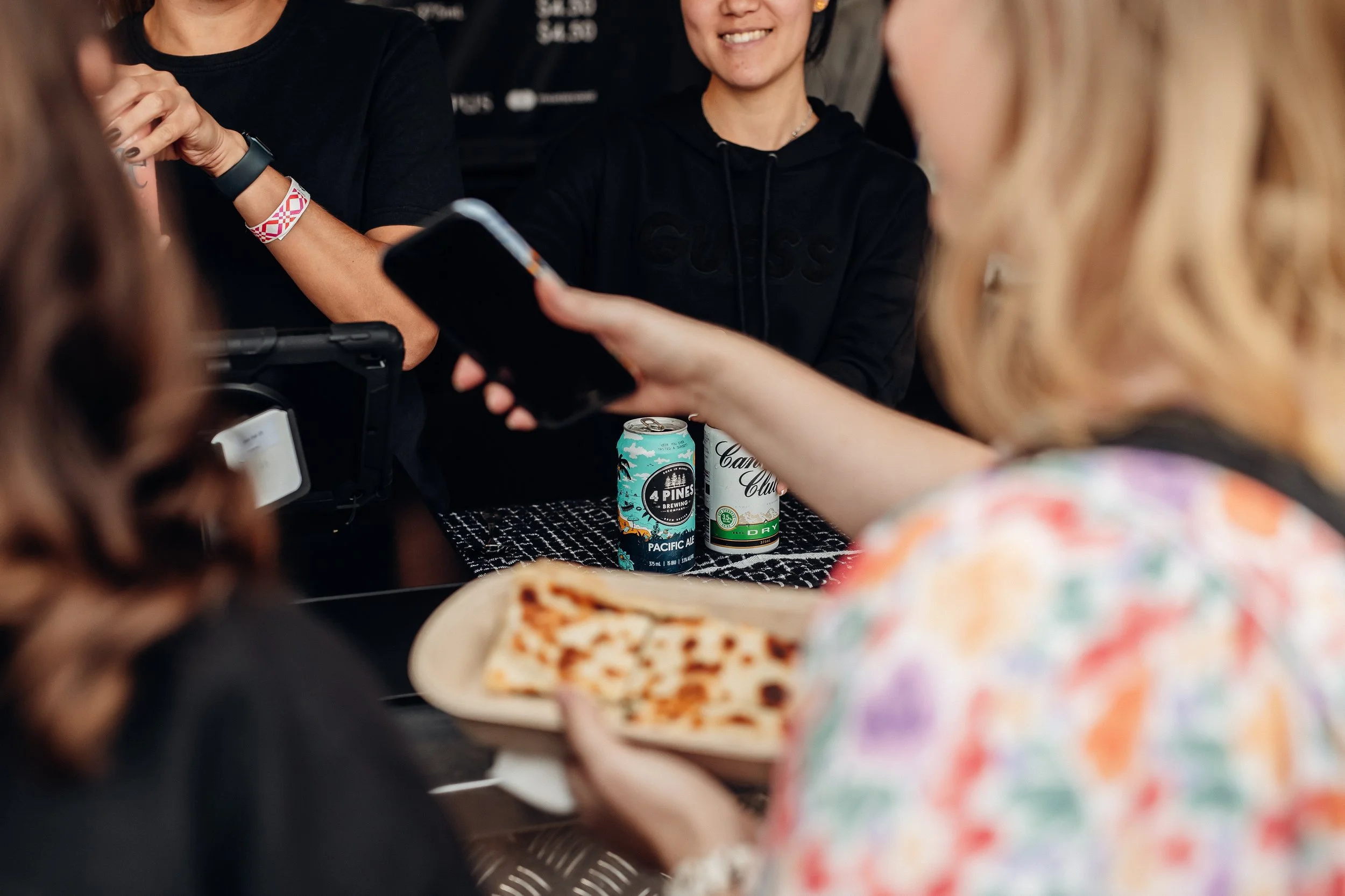 Bartenders behind a bar serving drinks. Customer in foreground holding gozleme.