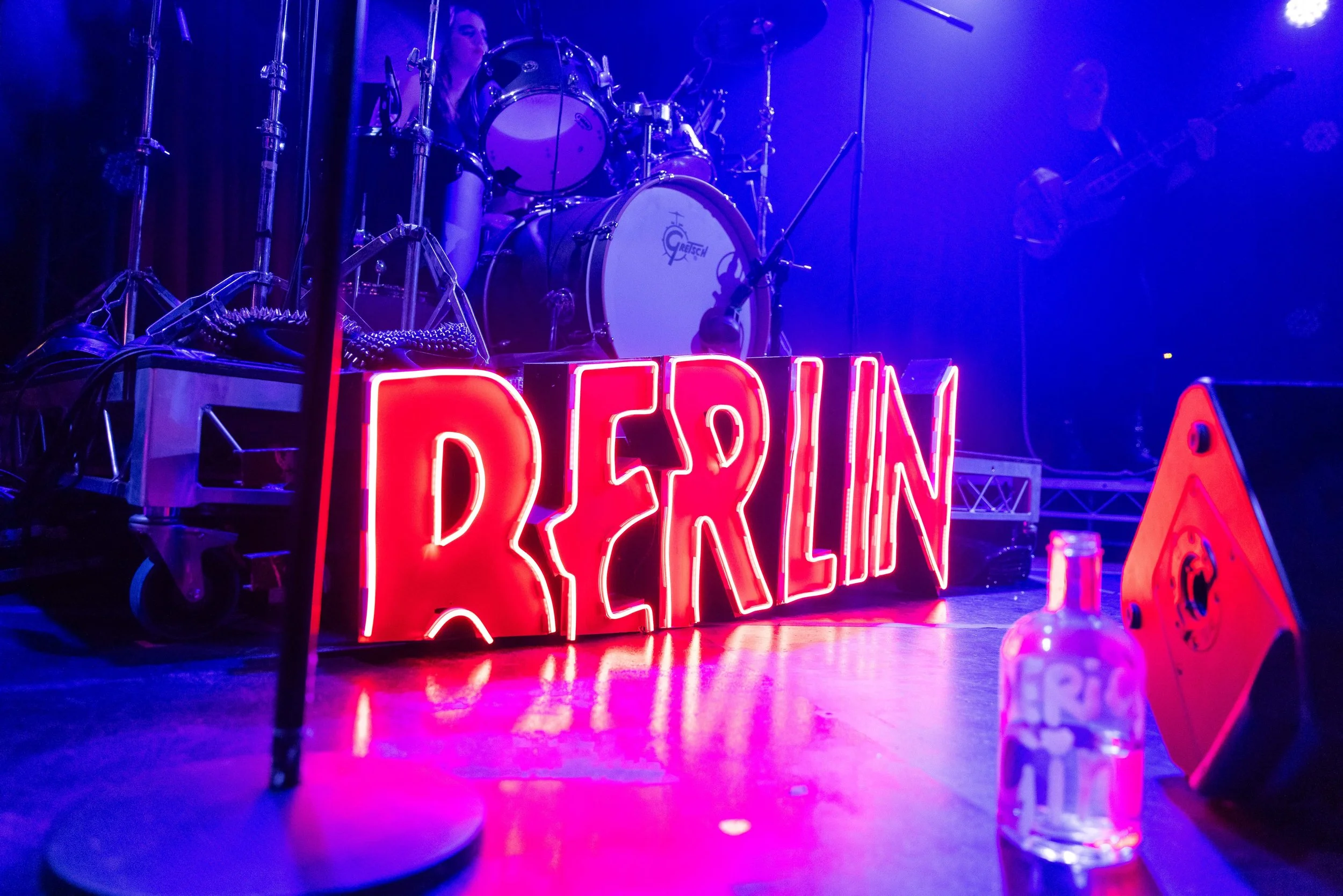 Neon sign on stage saying Berlin, with drums behind.